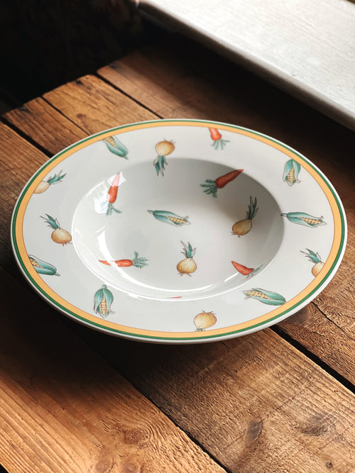 Angled side view of a Villeroy & Boch A La Ferme rimmed soup bowl on a rustic wood surface