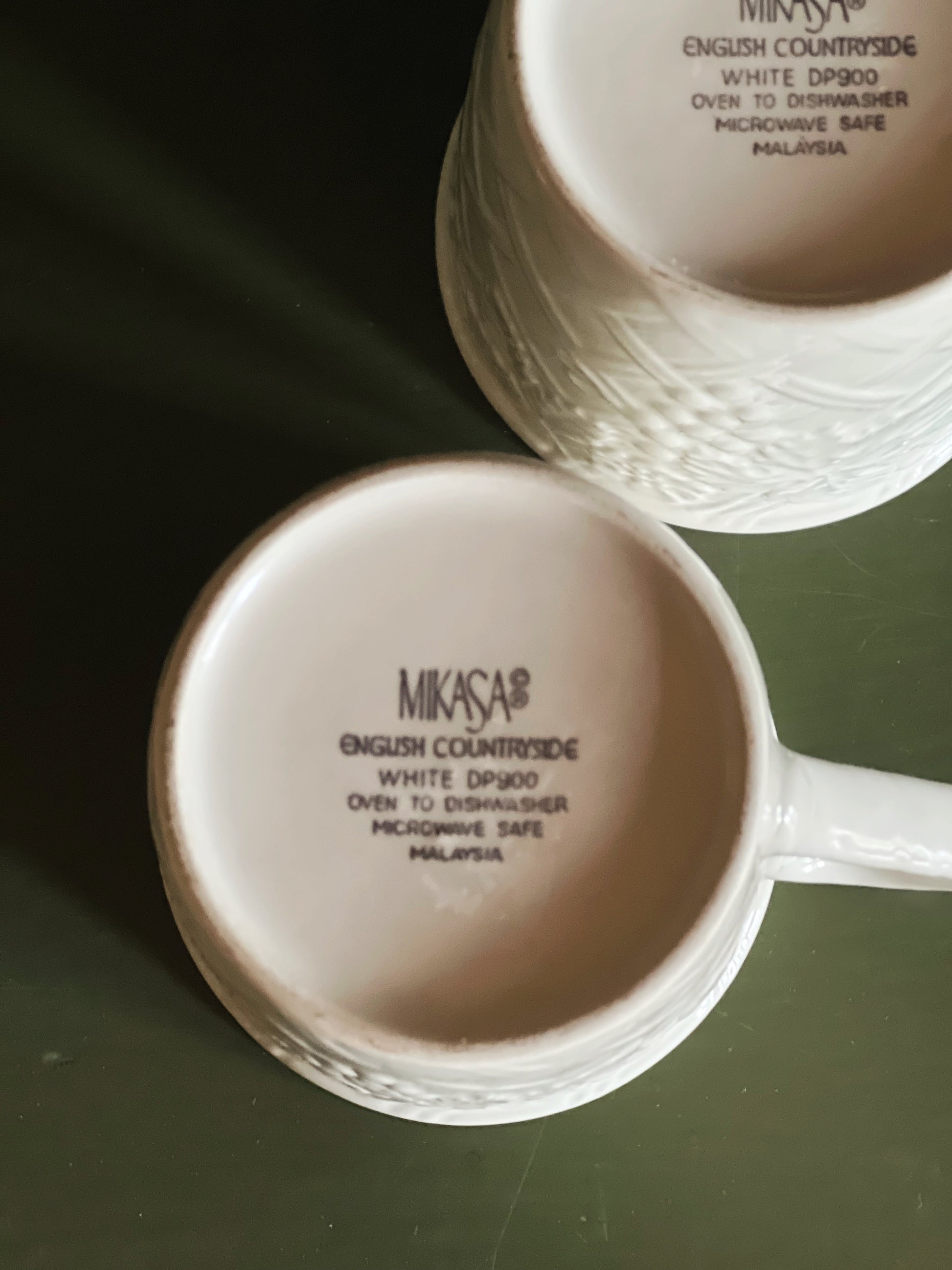 Two white mugs with 'Mikasa' branding on a dark surface