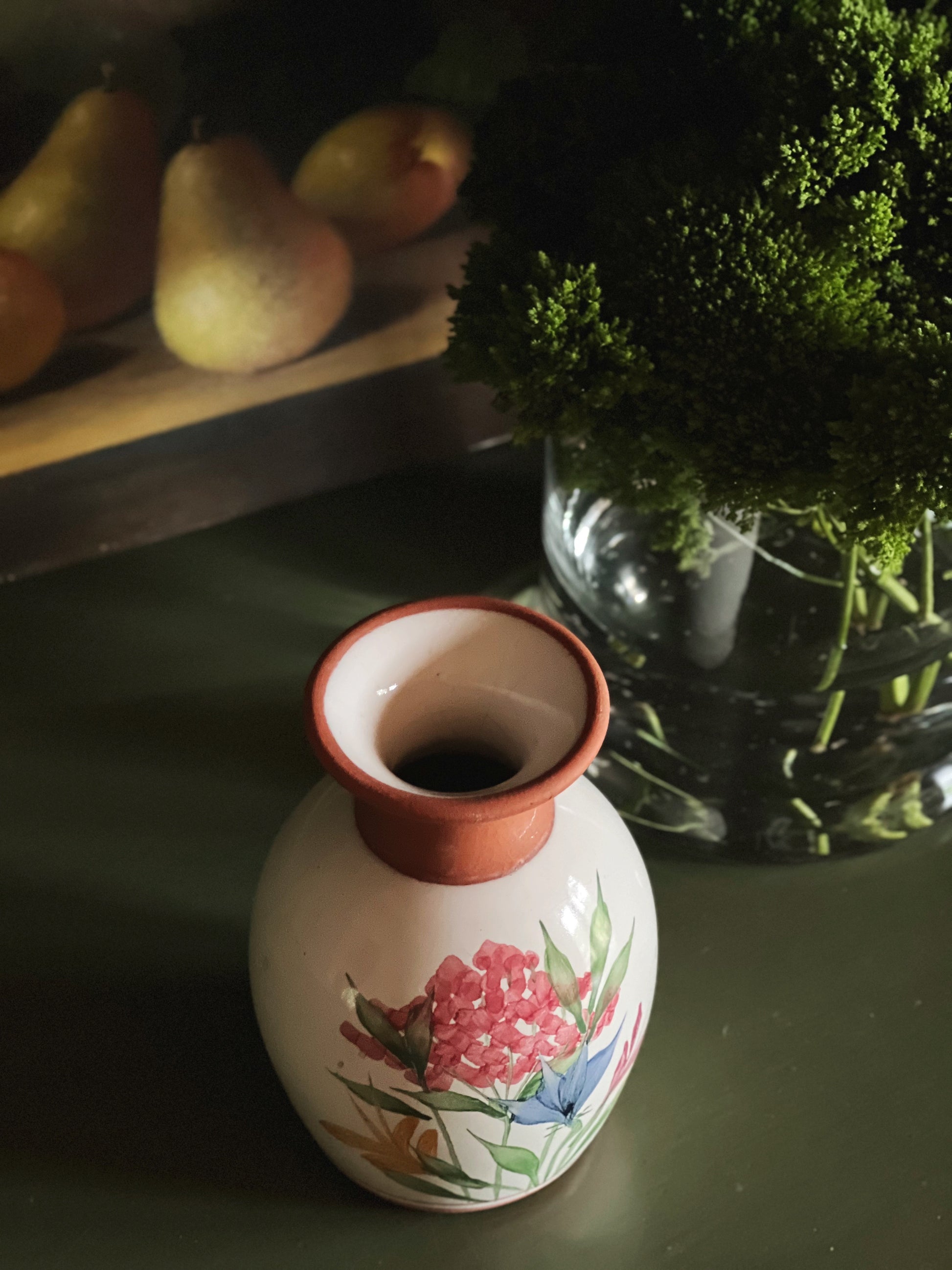 Overhead angle of a small handmade pottery vase next to a floral arrangement and a moody still life painting
