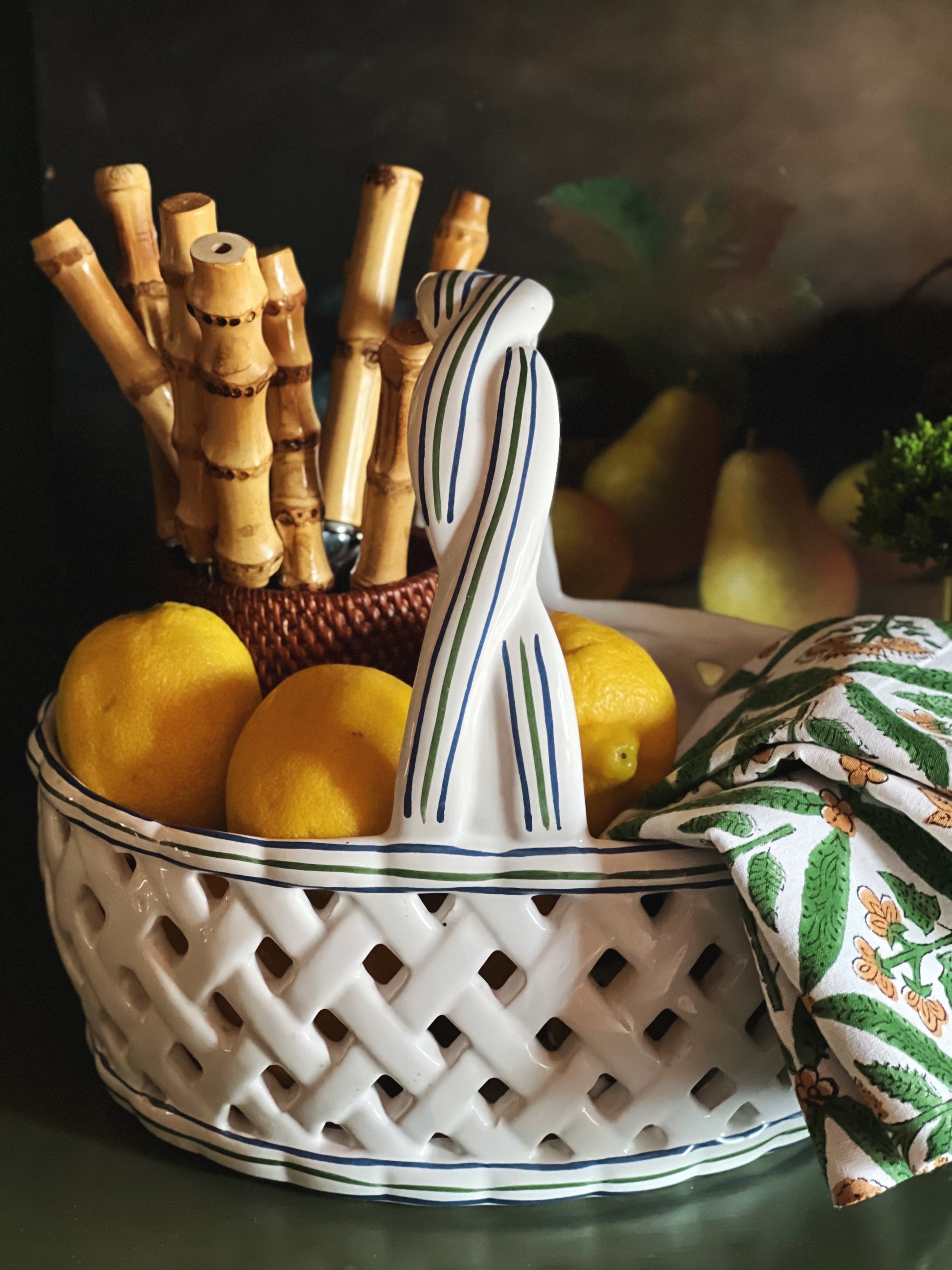 White ceramic basket with decorative handle, lemons, and a bamboo holder on a dark background