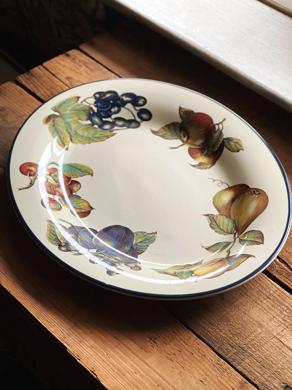 full view of a serving platter with fruit and leaf design on a wooden surface