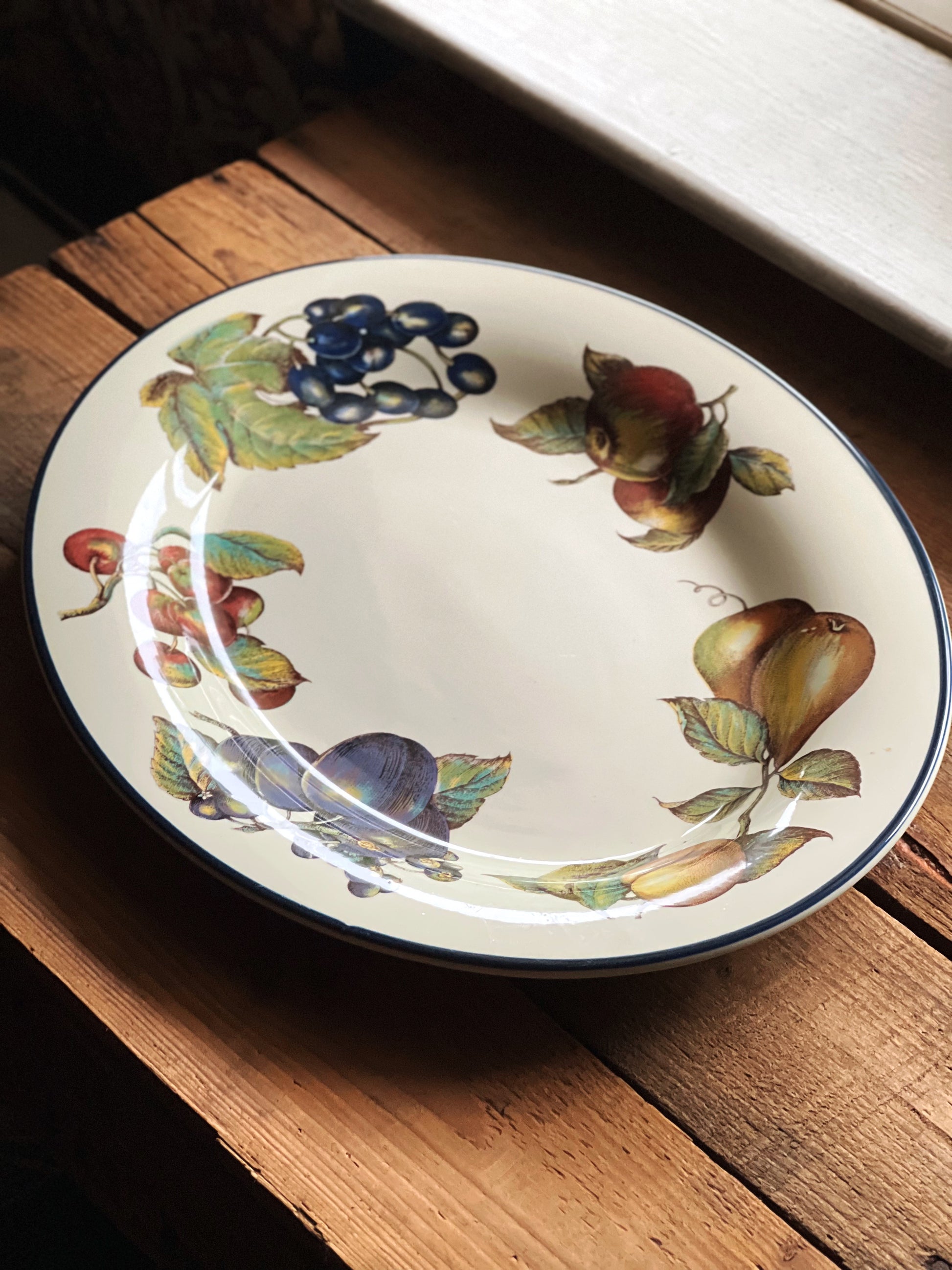 full view of a serving platter with fruit and leaf design on a wooden surface