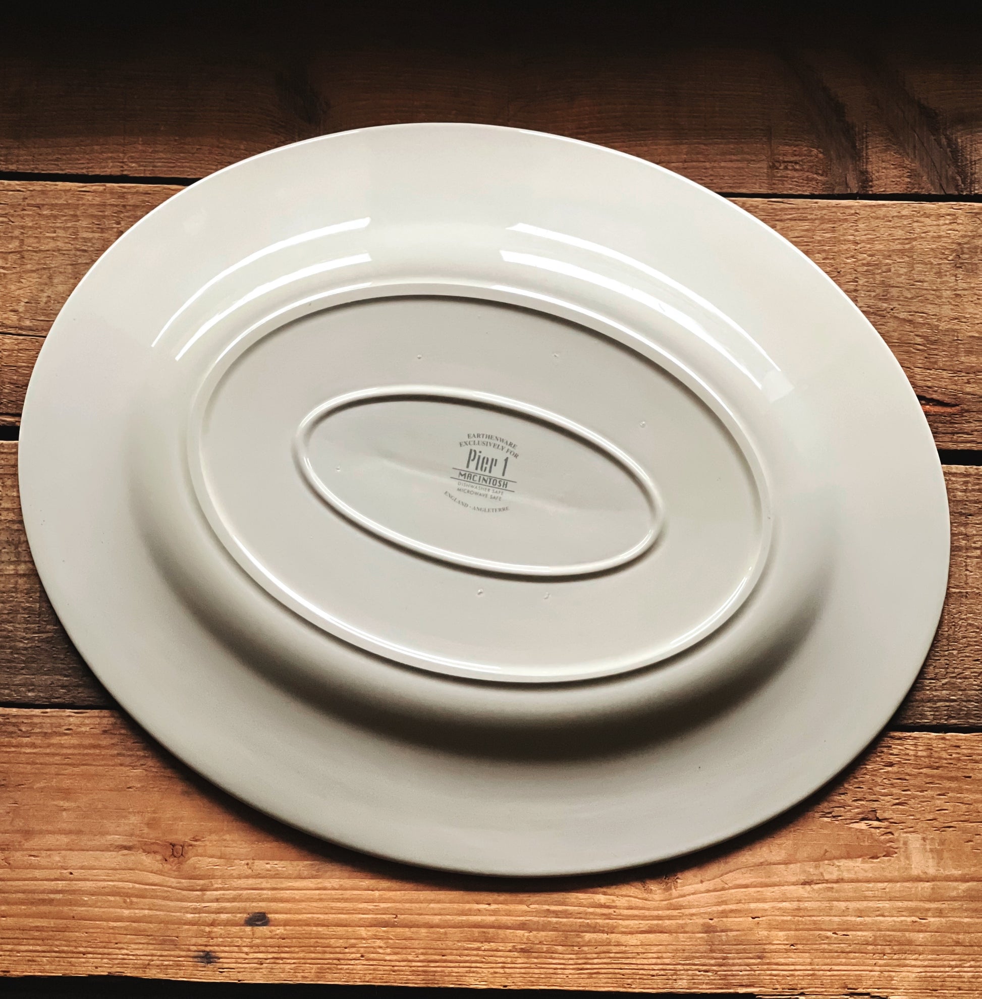 Underside of an oval serving platter with 'Pier 1' branding on a wooden surface