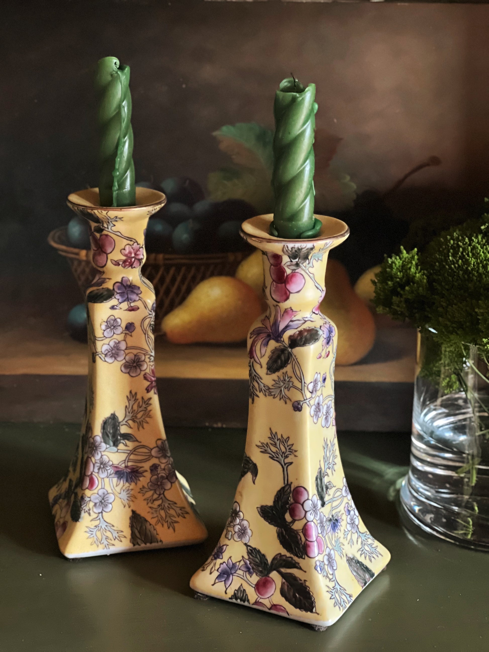 Pair of vintage floral porcelain candlesticks with green taper candles styled on a dark vintage table