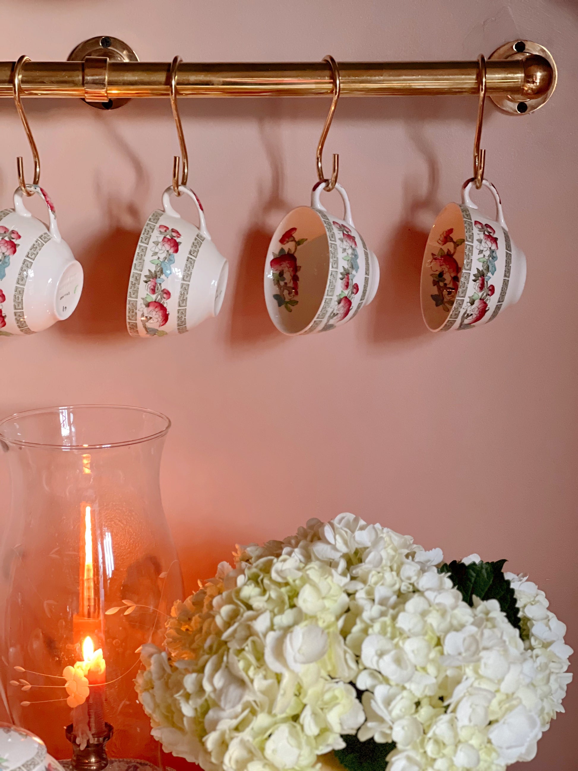 Vintage Indian Tree teacups hanging beneath brass rail in cottage-inspired kitchen