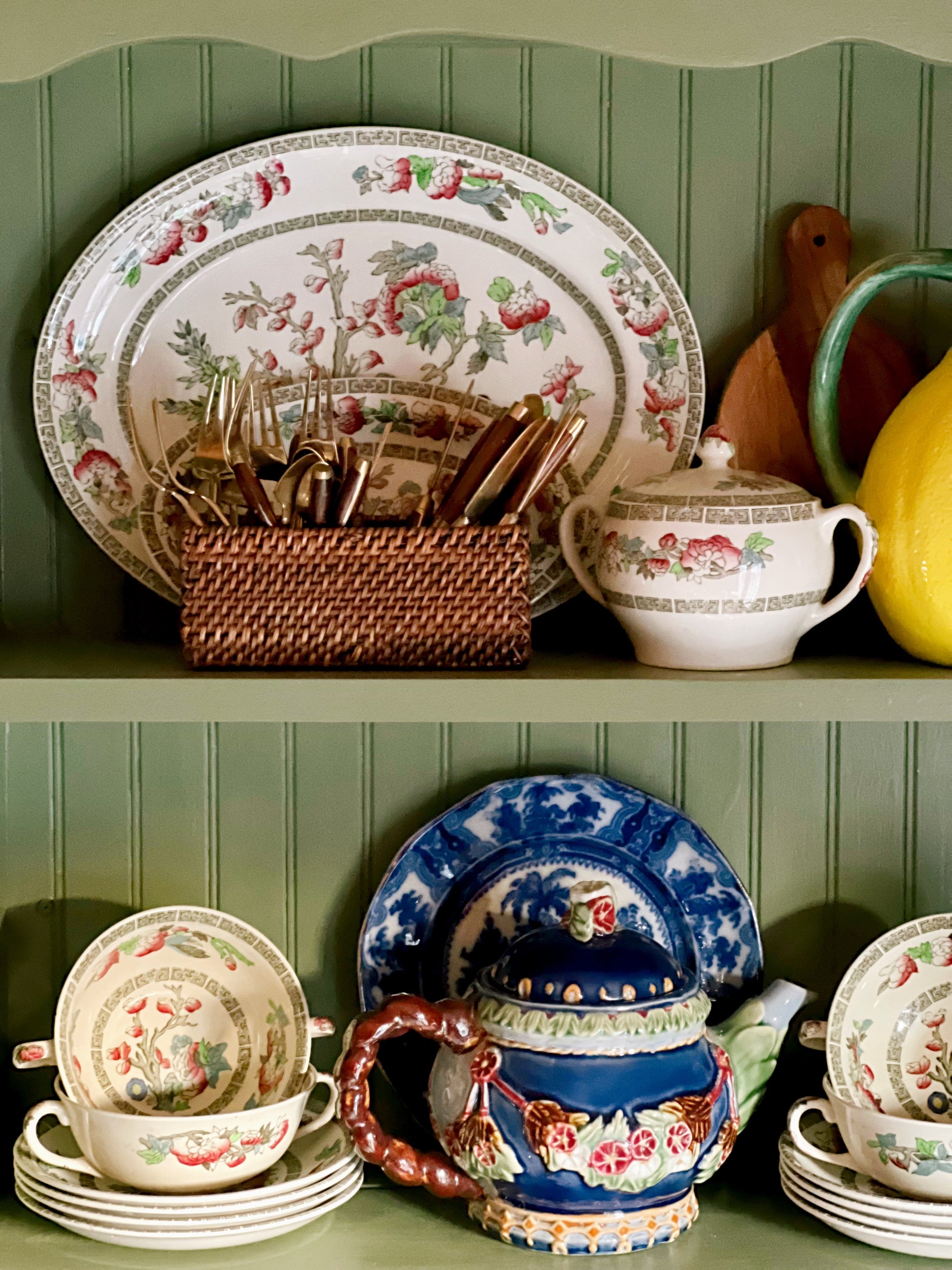 Vintage navy blue floral teapot displayed on green cabinet shelves with Indian Tree china