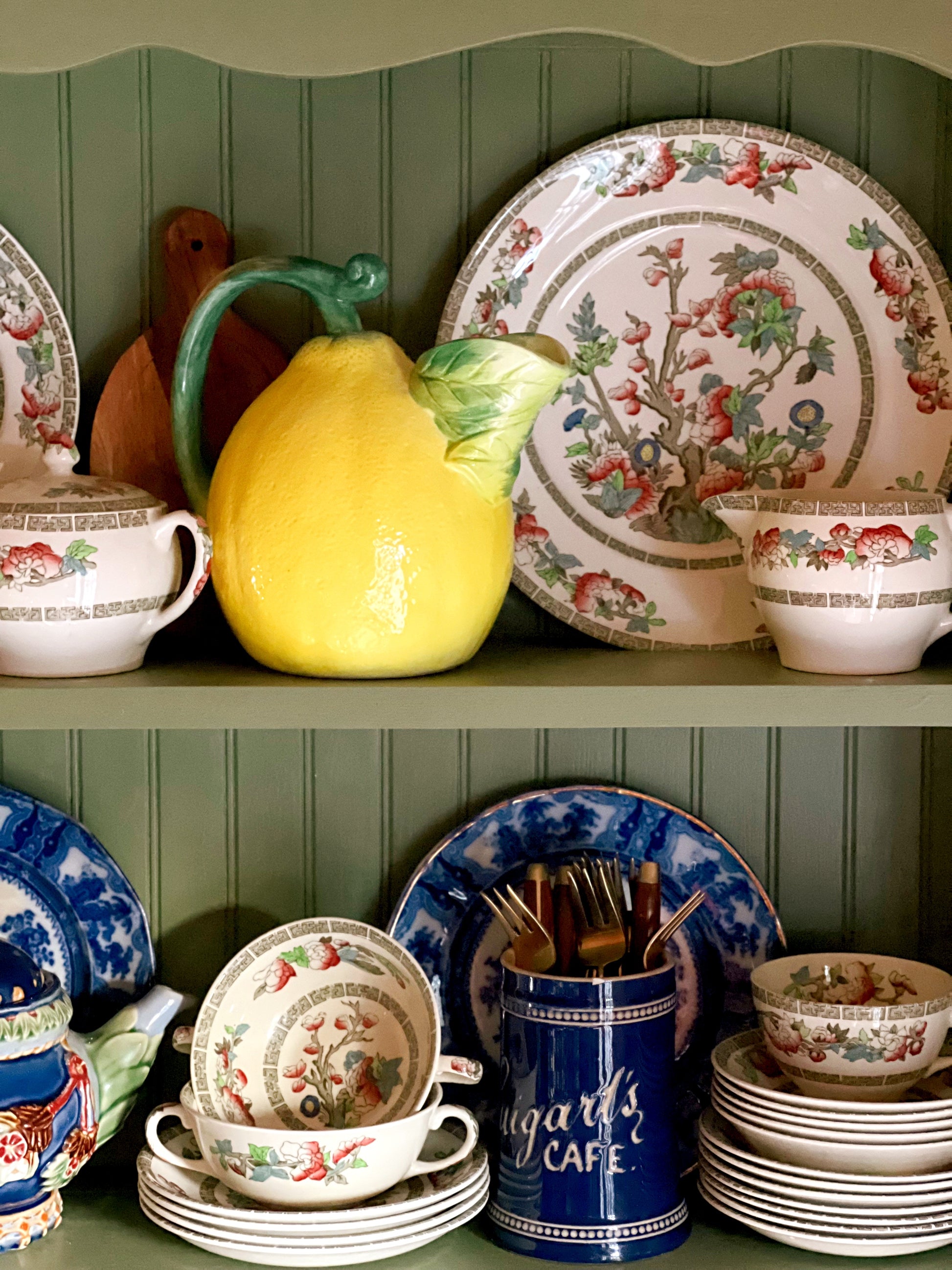 Vintage ceramic lemon pitcher styled on green cottage cabinet shelves with English transferware