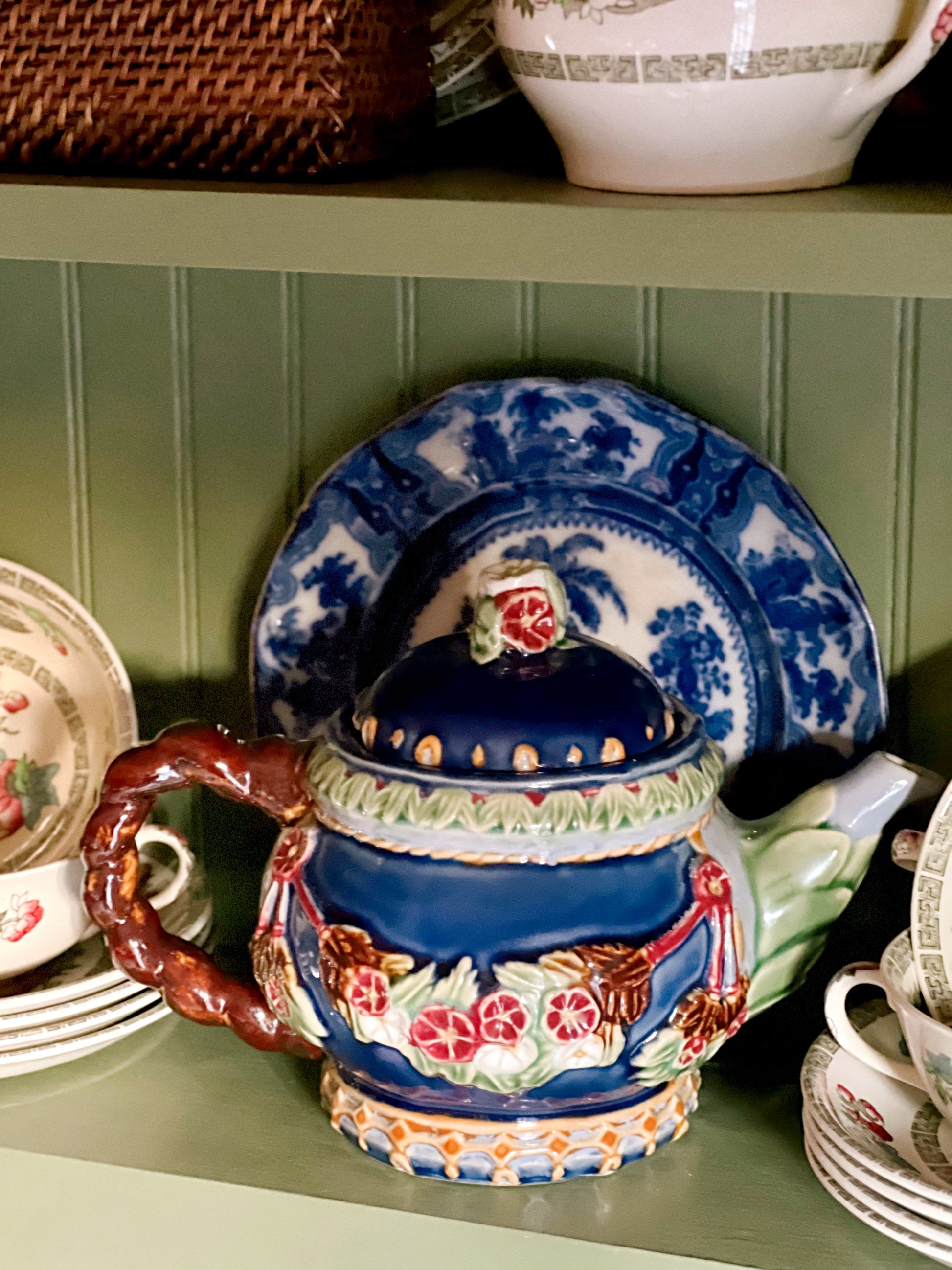 Vintage navy blue majolica style teapot styled in warm cottage kitchen lighting beside floral tableware