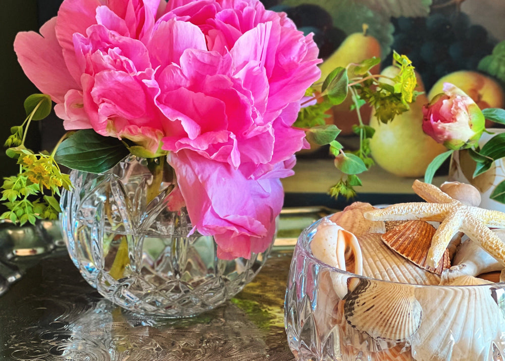 Vase of pink flowers on a decorative tray with a painting in the background