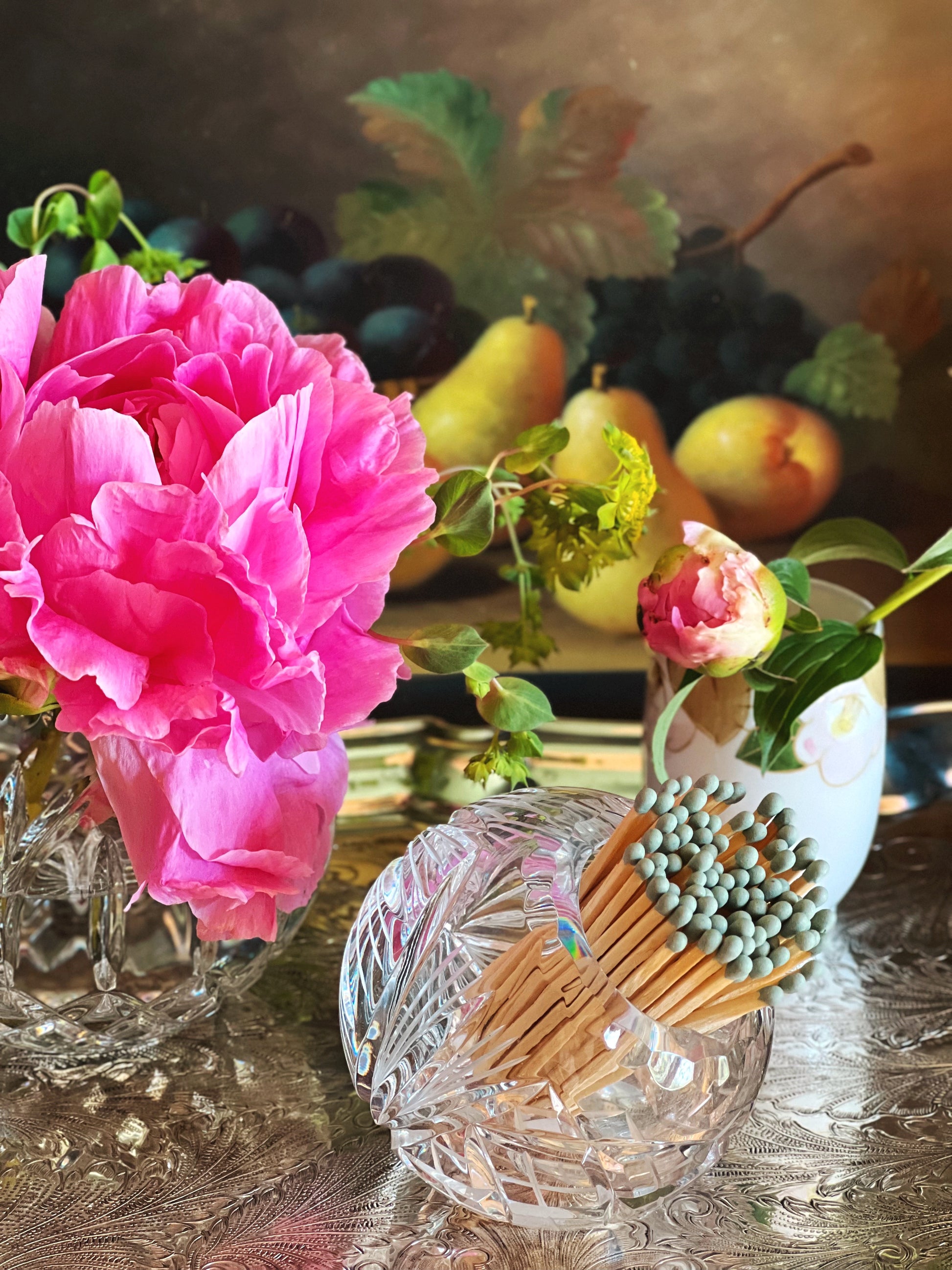 side view of a crystal holder with wooden matches and pink flowers on a reflective surface