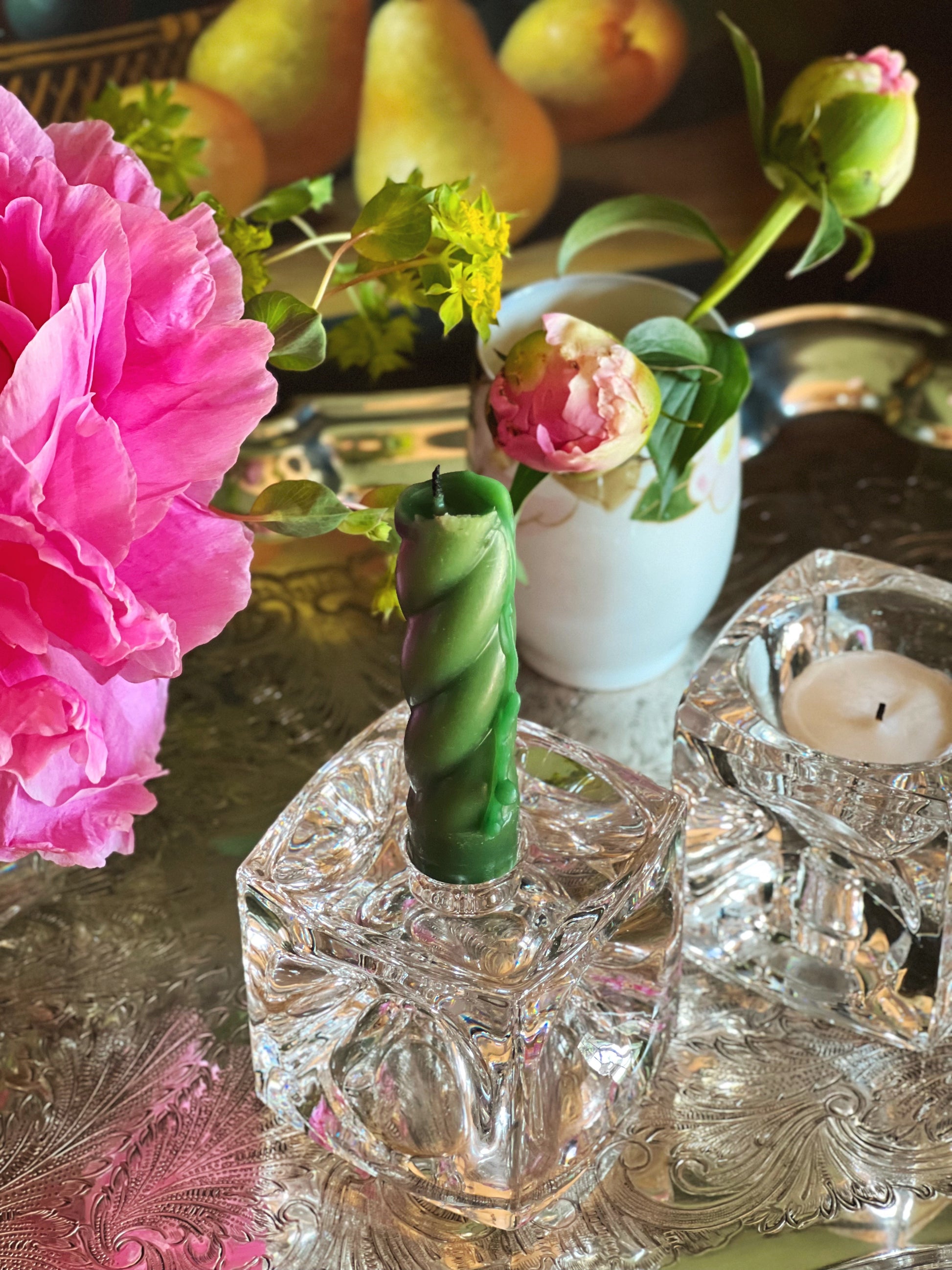 Decorative candle with a green spiral design on a crystal holder, surrounded by pink flowers and pears.
