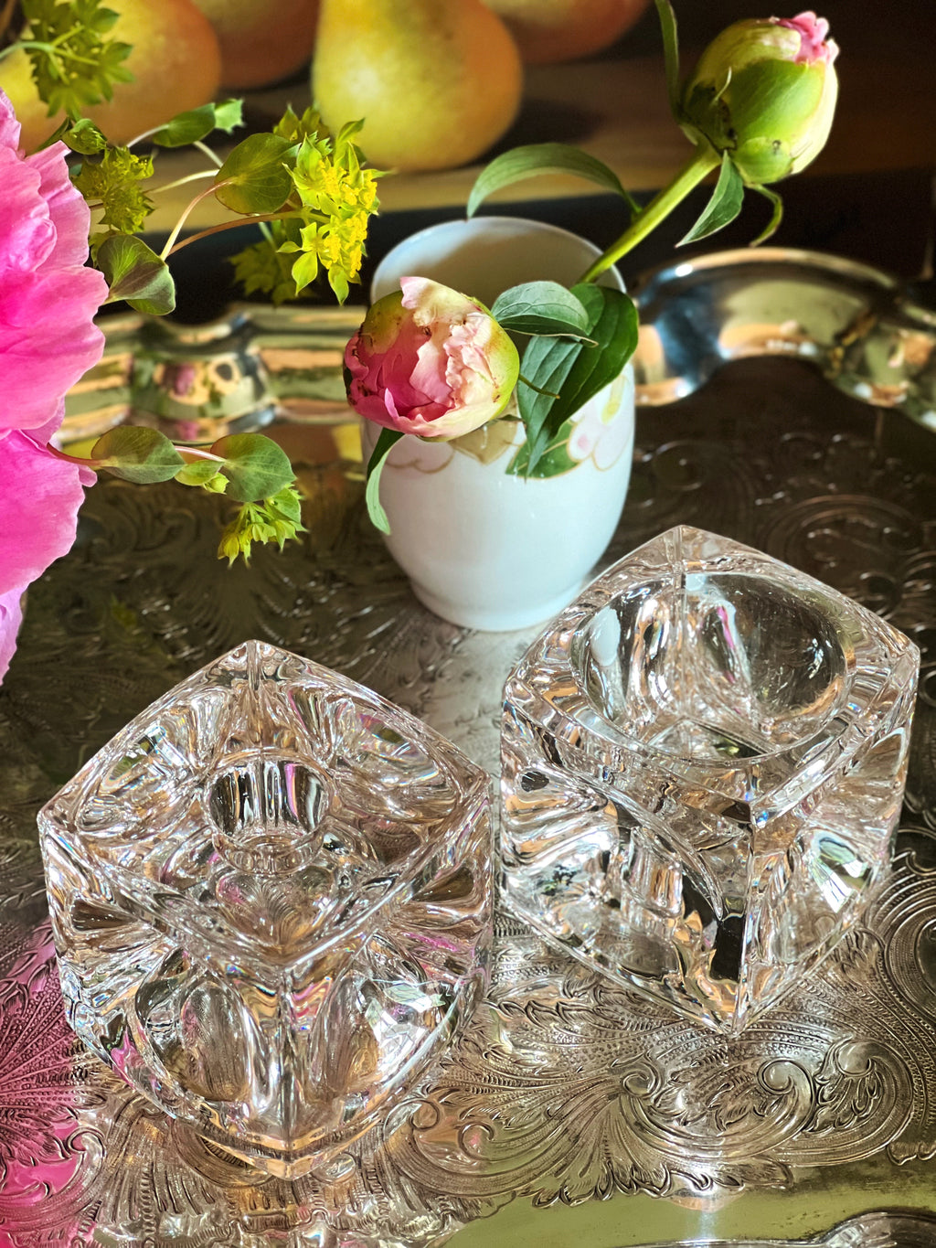 Overhead view of two crystal coasters on a reflective surface with flowers and fruit in the background.