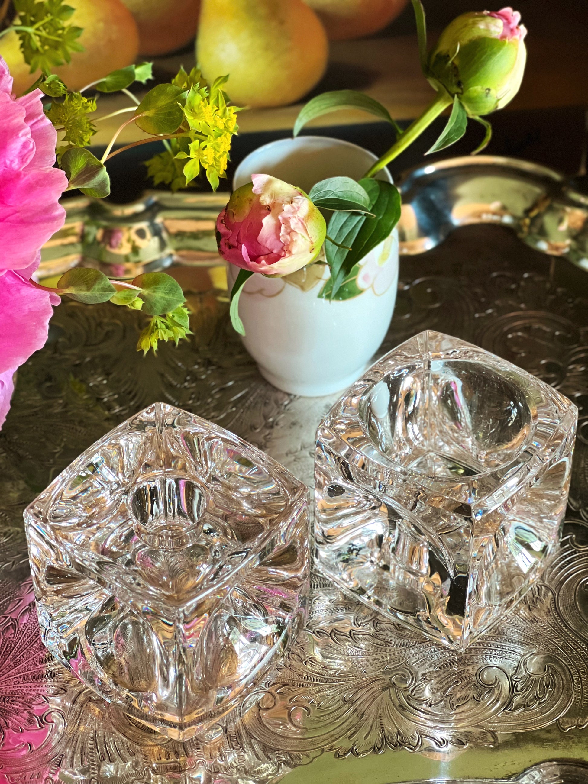 Overhead view of two crystal coasters on a reflective surface with flowers and fruit in the background.