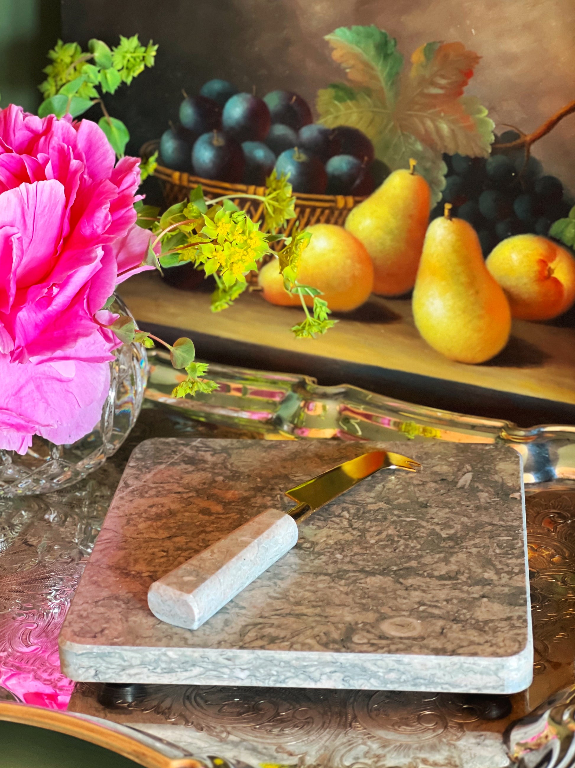 Still life arrangement with fruits, flowers, and a marble cutting board.