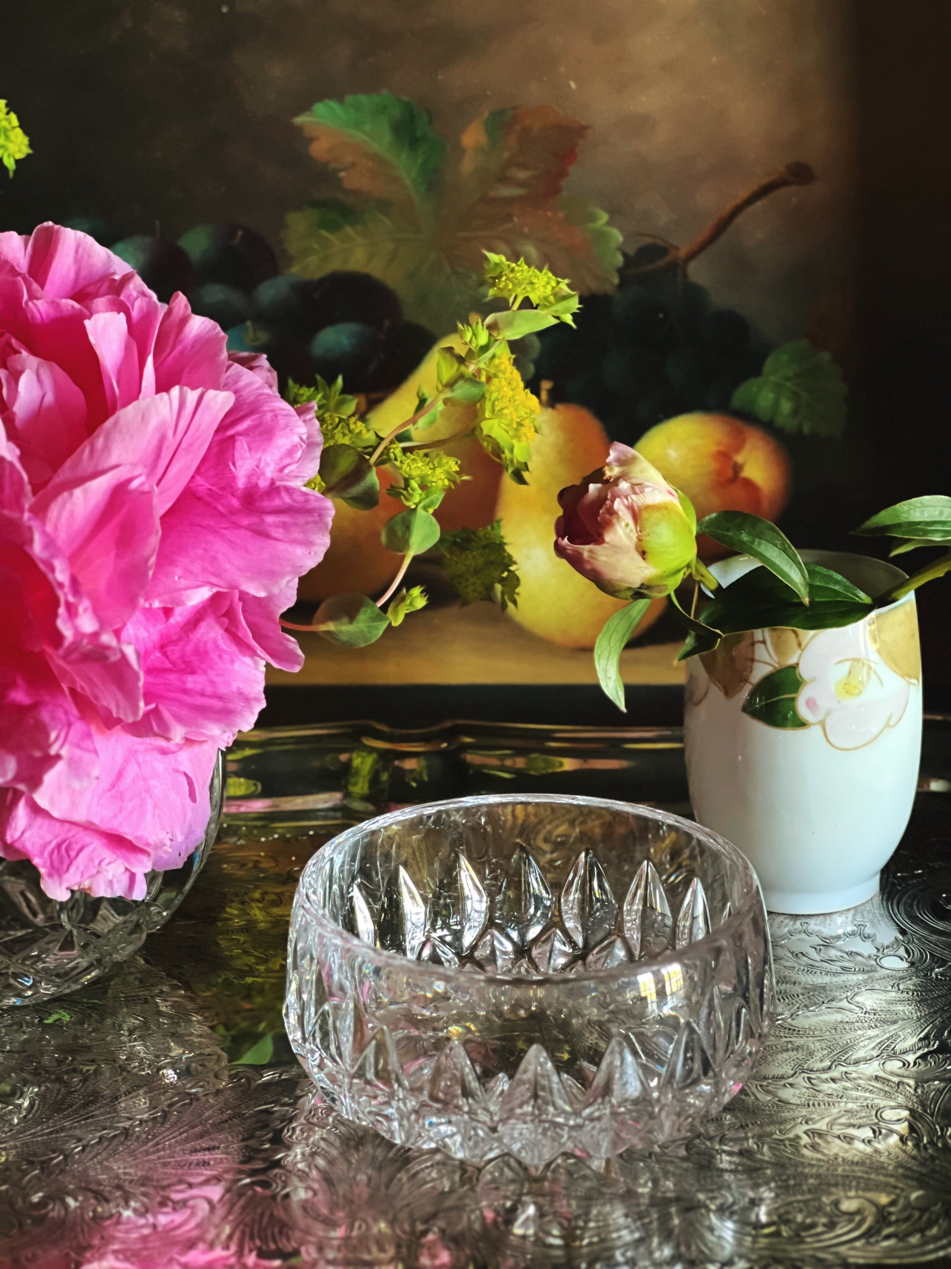 Pink flower, glass bowl, and fruit on a silver surface