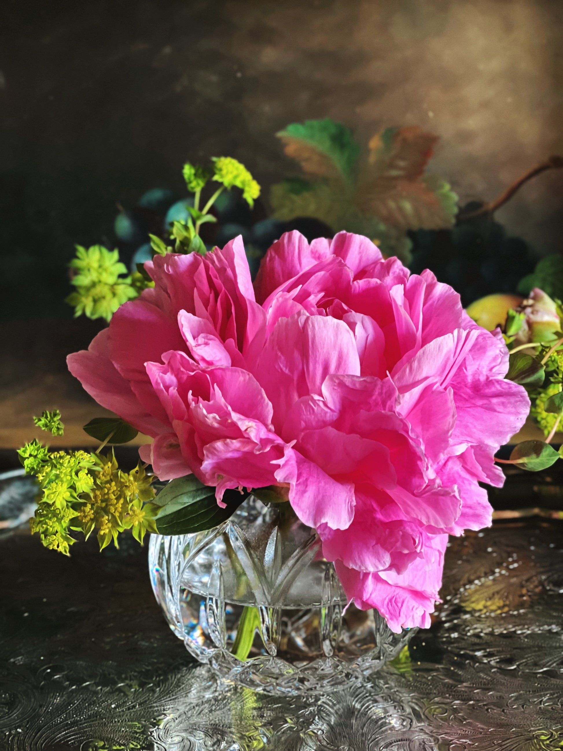 Pink peony flower in a crystal vase on a reflective surface with a blurred background