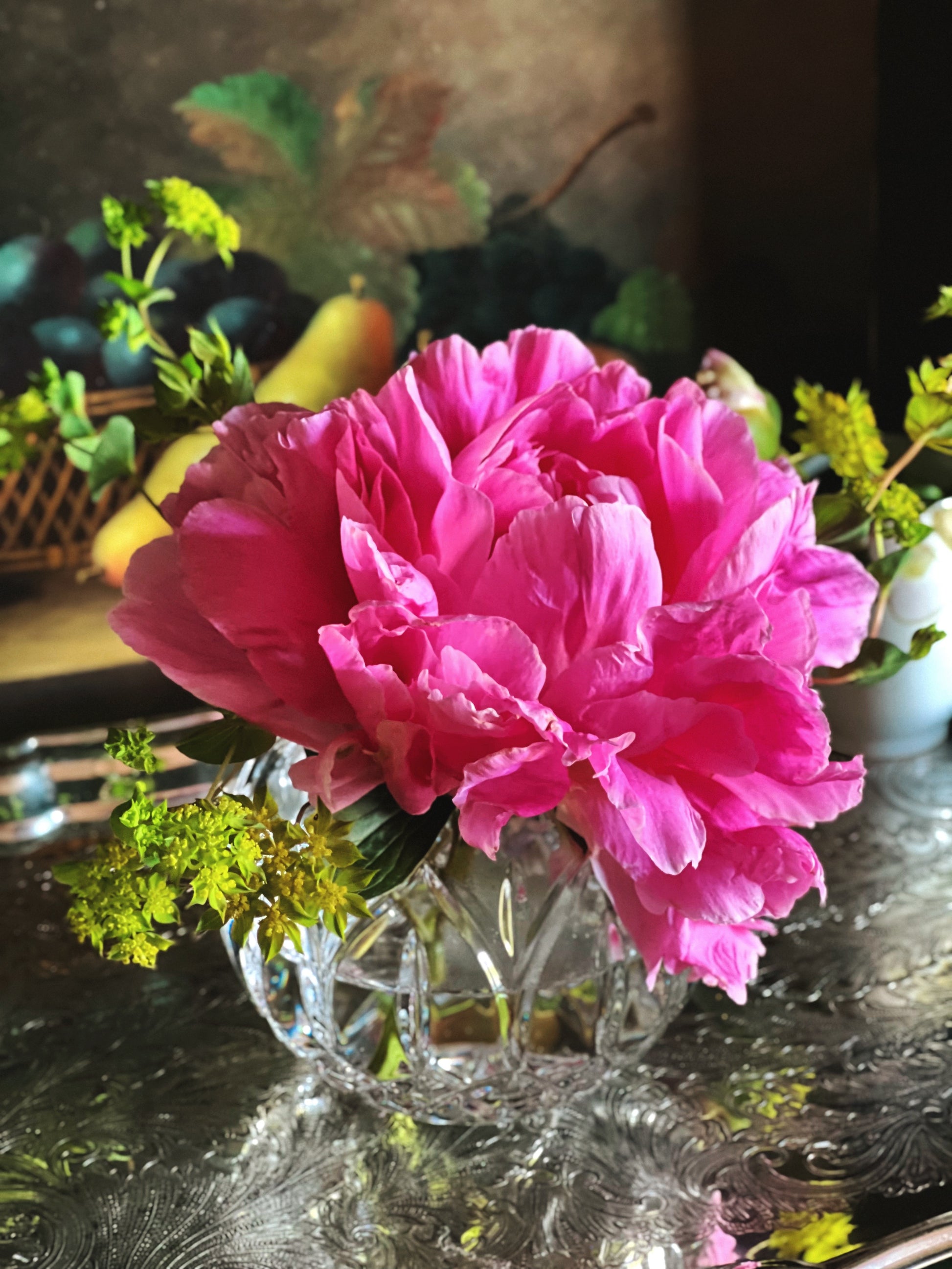 Side view of a pink peonyflowers in a clear glass vase on a reflective surface with blurred background