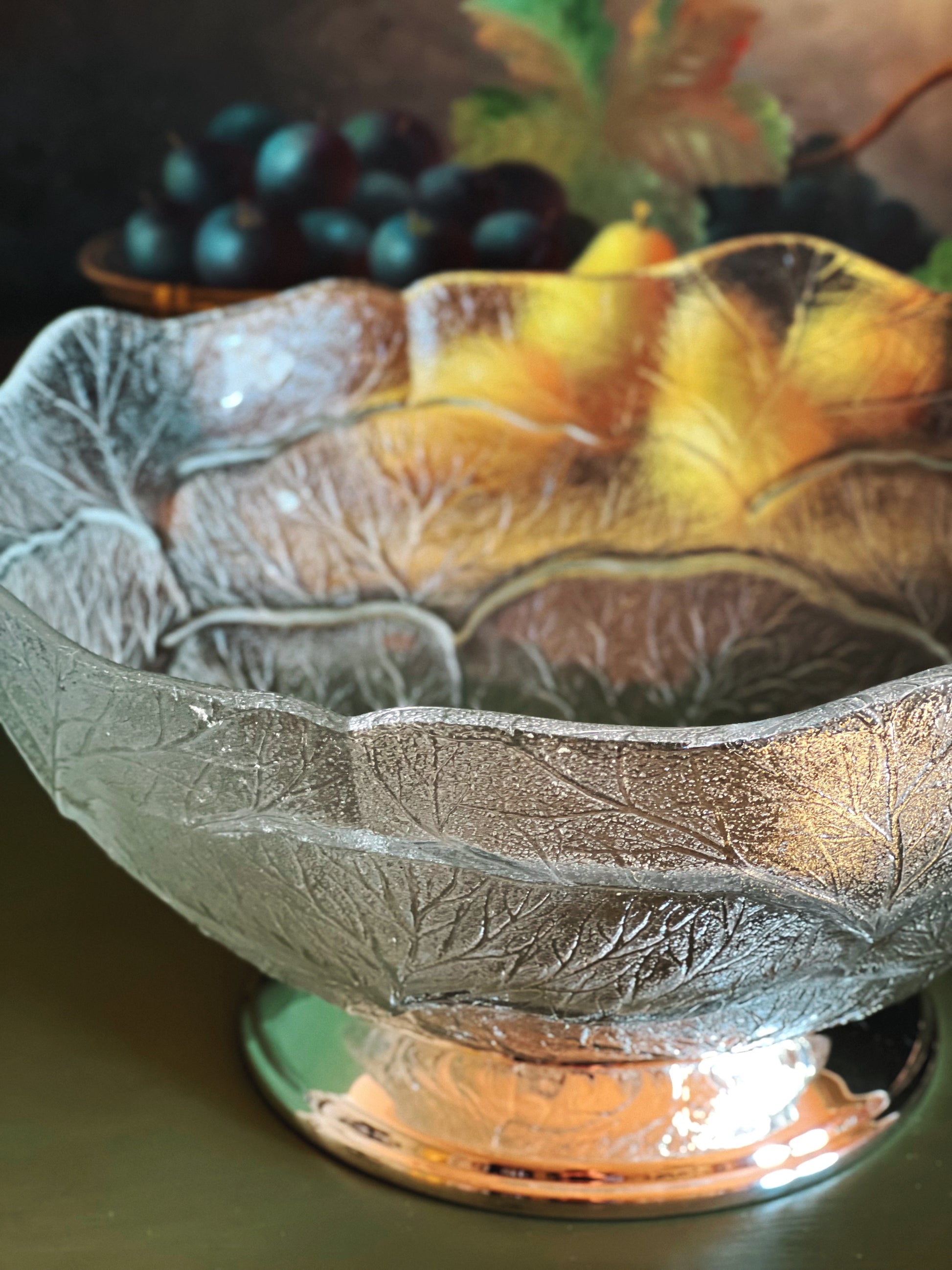 Decorative glass bowl with leaf patterns containing fruits on a dark background