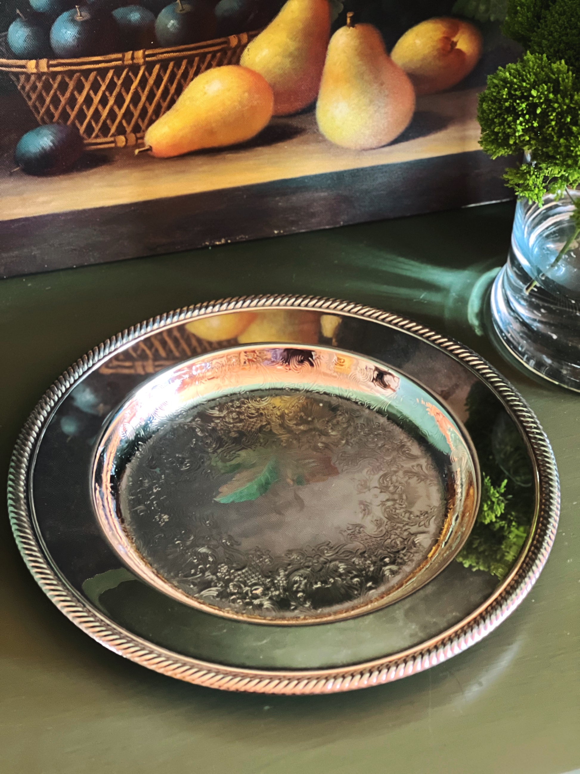 Overhead angle of a Wm Rogers silver tray on a green surface with pears and a basket in the background