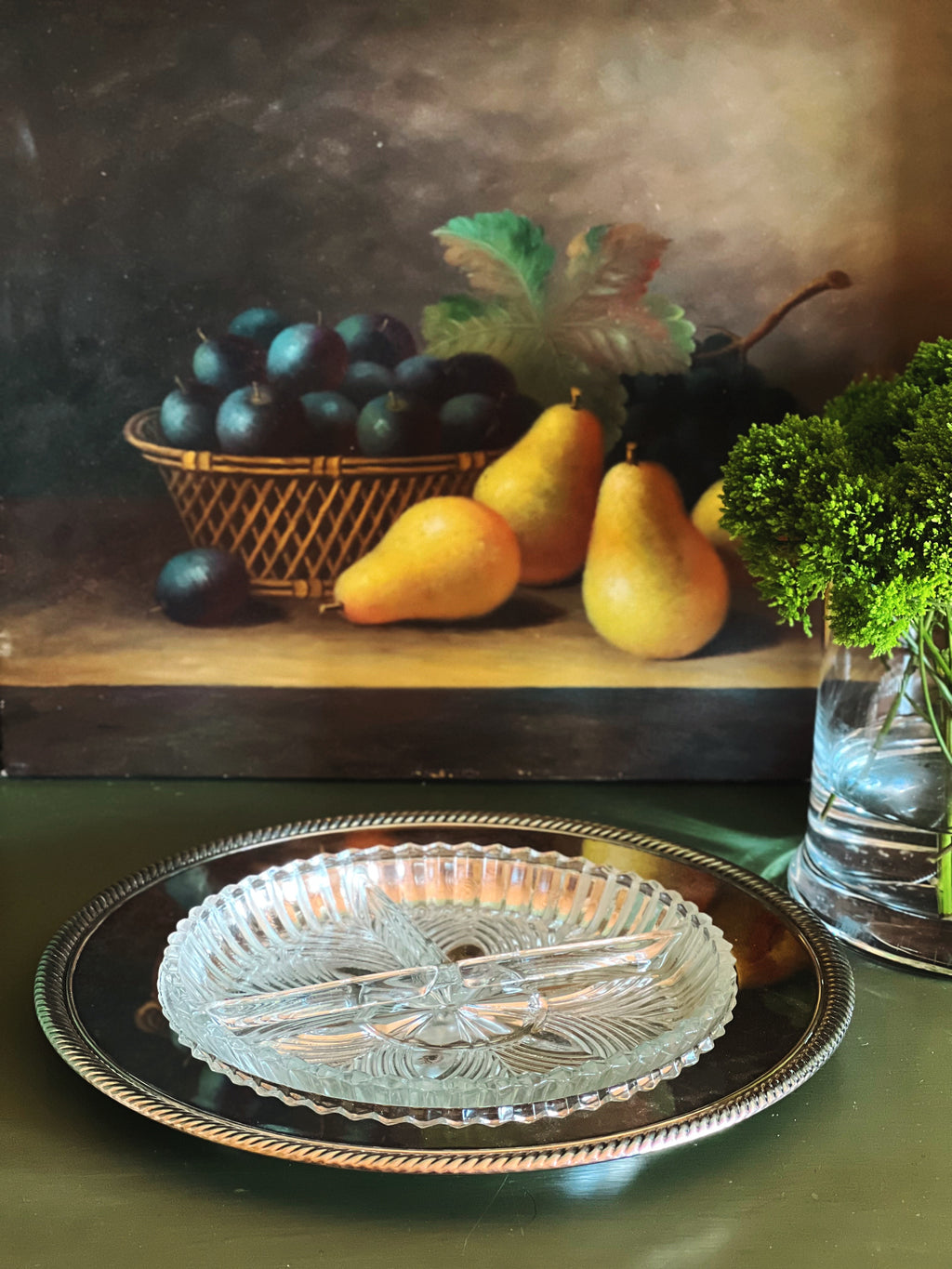 Still life painting of fruits and a glass dish on a table.