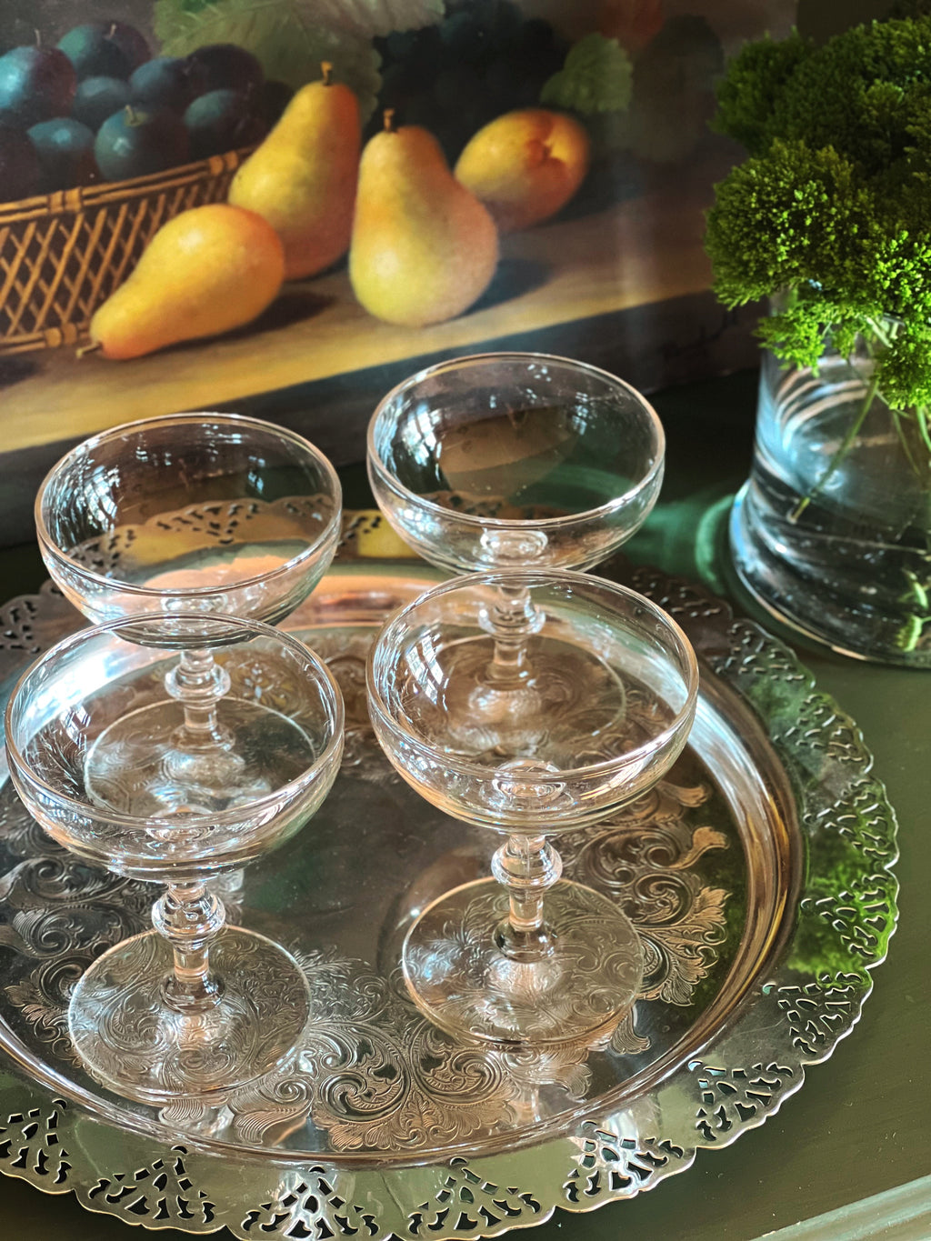 Overhead angle of a set of four vintage champagne coupes with bamboo-style stems displayed on a silver tray with pears and greenery