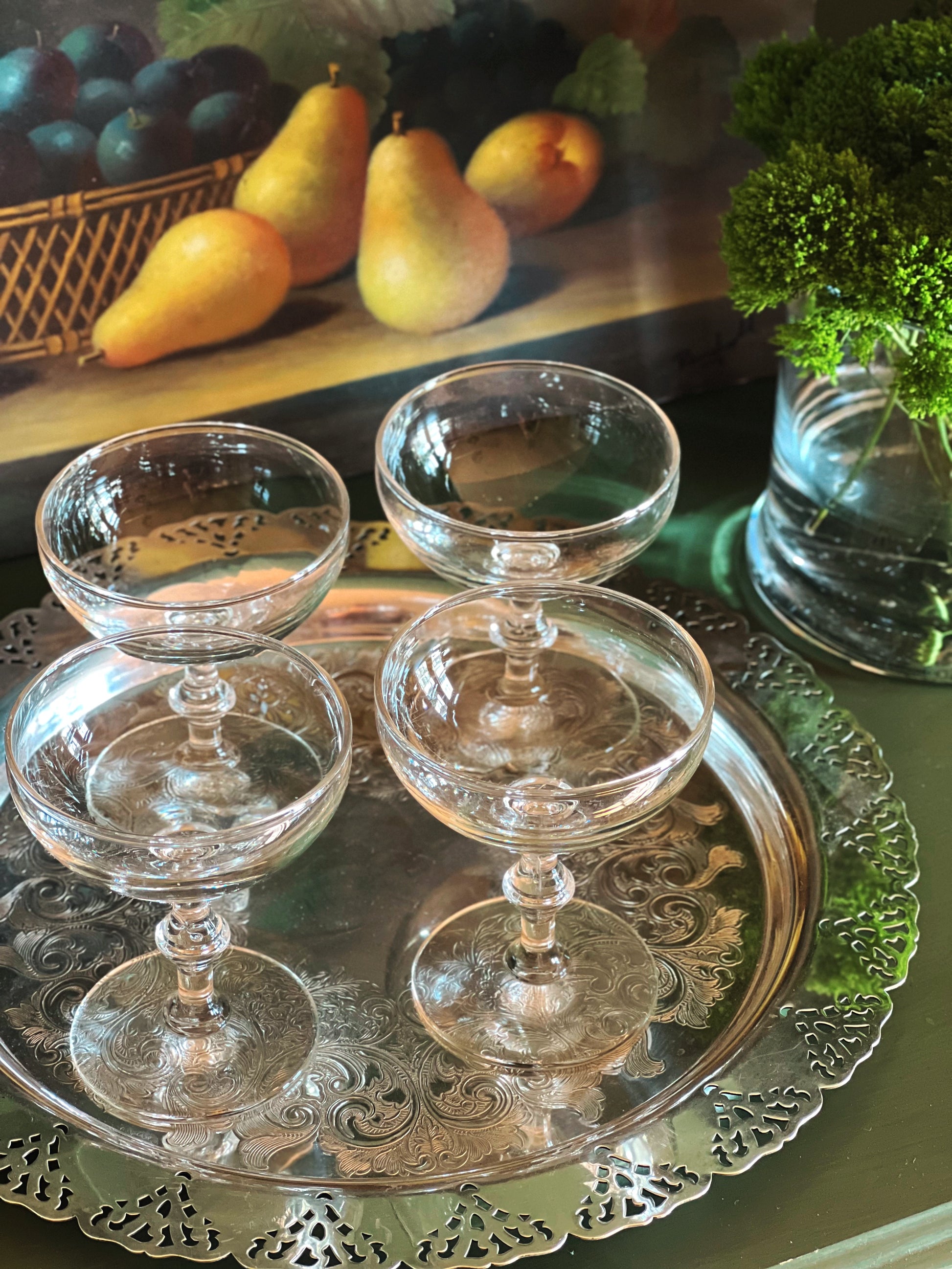 Overhead angle of a set of four vintage champagne coupes with bamboo-style stems displayed on a silver tray with pears and greenery