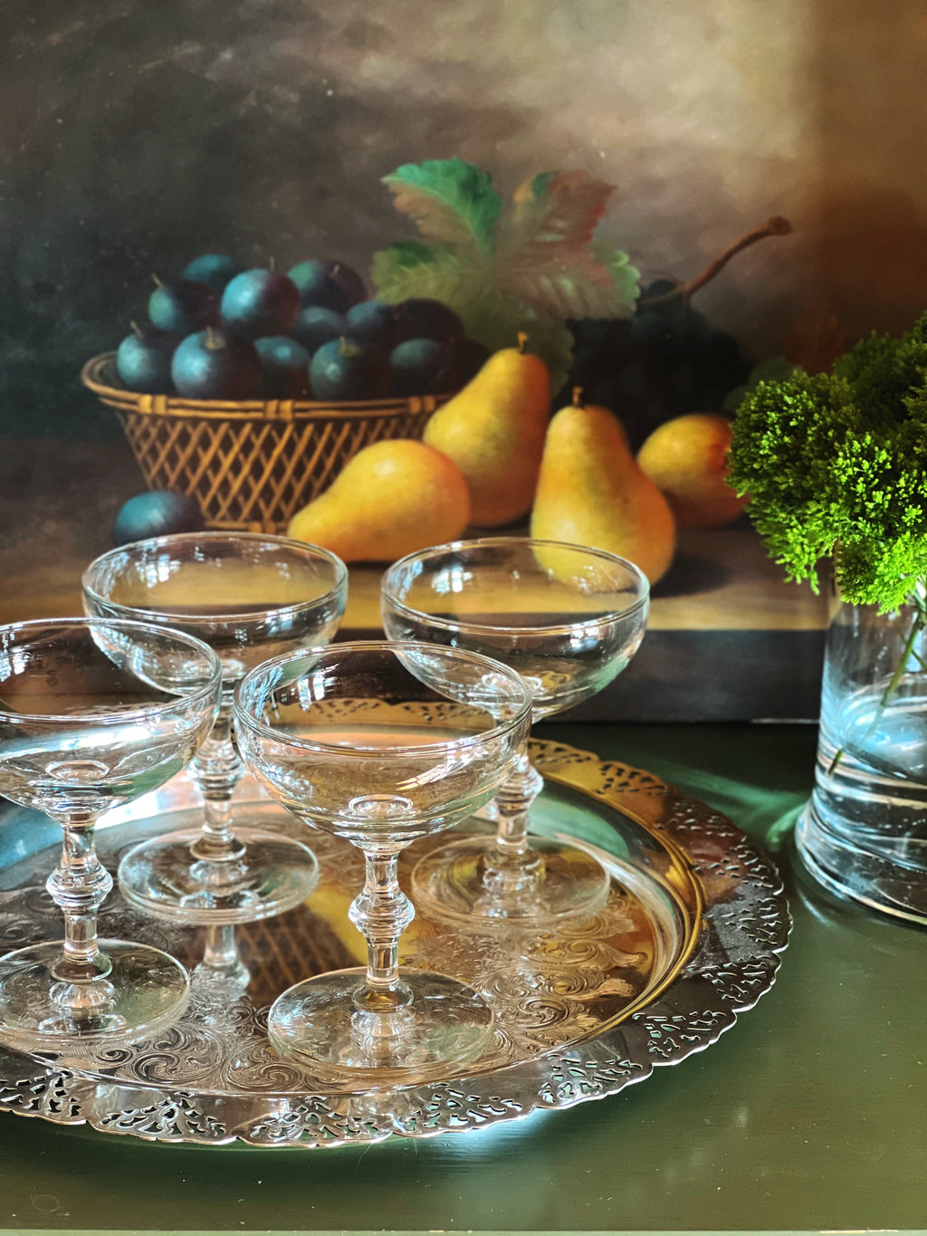 Set of four vintage champagne coupes with bamboo-style stems displayed on a silver tray with pears and greenery