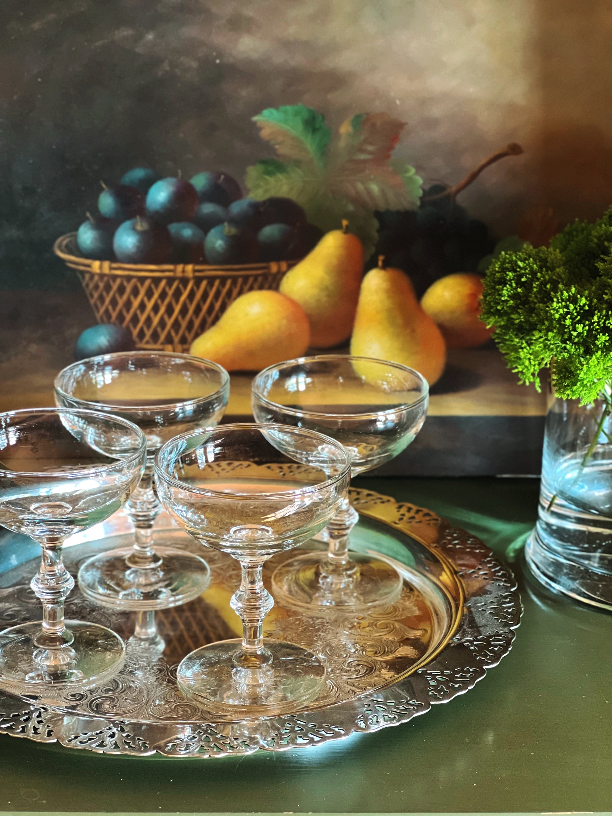 Set of four vintage champagne coupes with bamboo-style stems displayed on a silver tray with pears and greenery