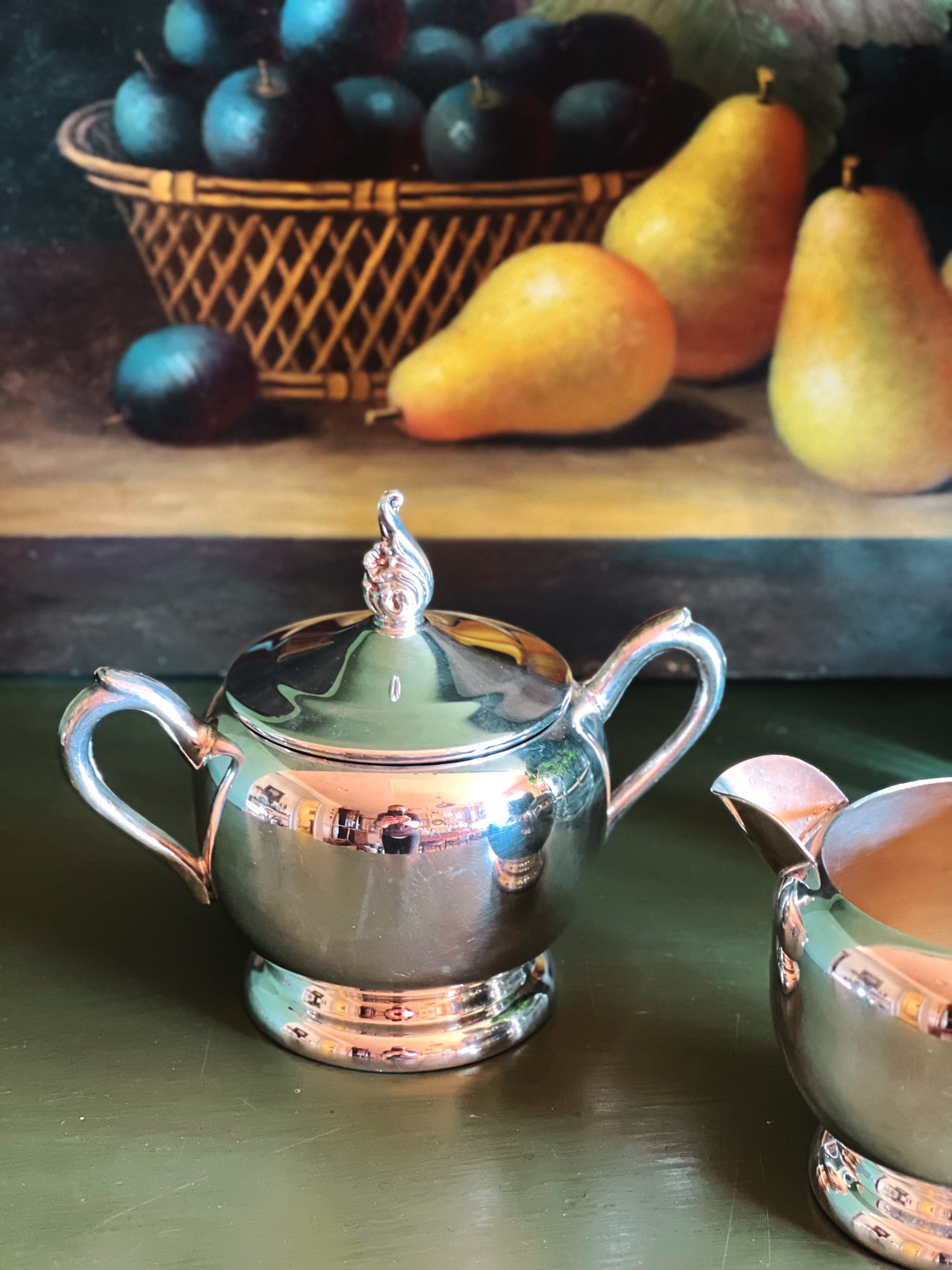 Silver FB Rogers sugar bowl with lid on a wooden surface with fruits in the background