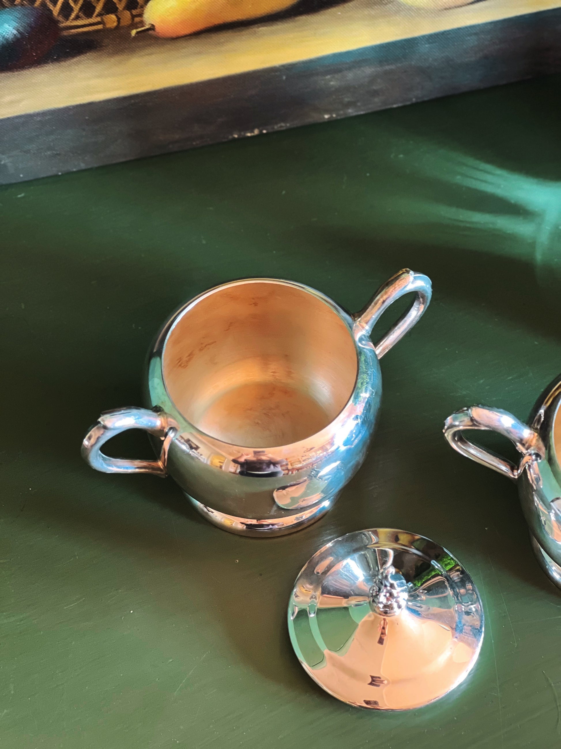 Overhead view of a silver sugar bowl with handle and lid on a green surface
