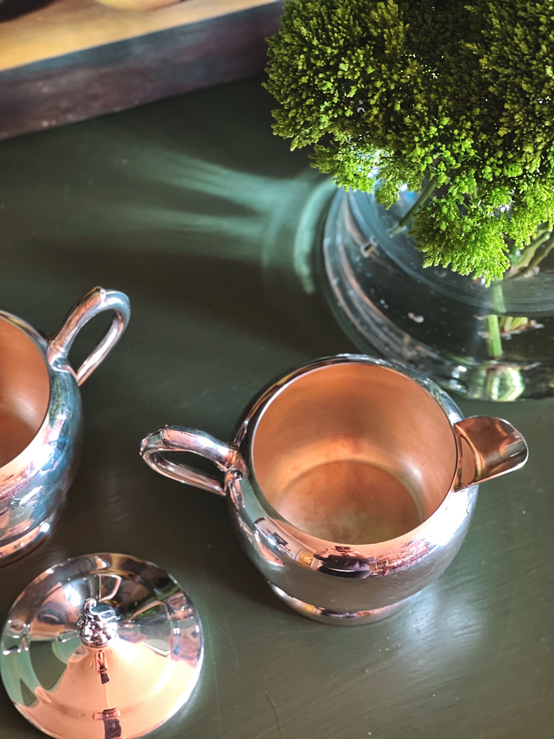 Overhead view of a silver creamer on a reflective surface with a vase in the background