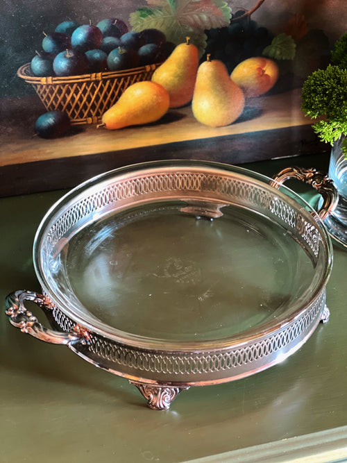 Decorative silver tray on a green surface with a still life painting in the background