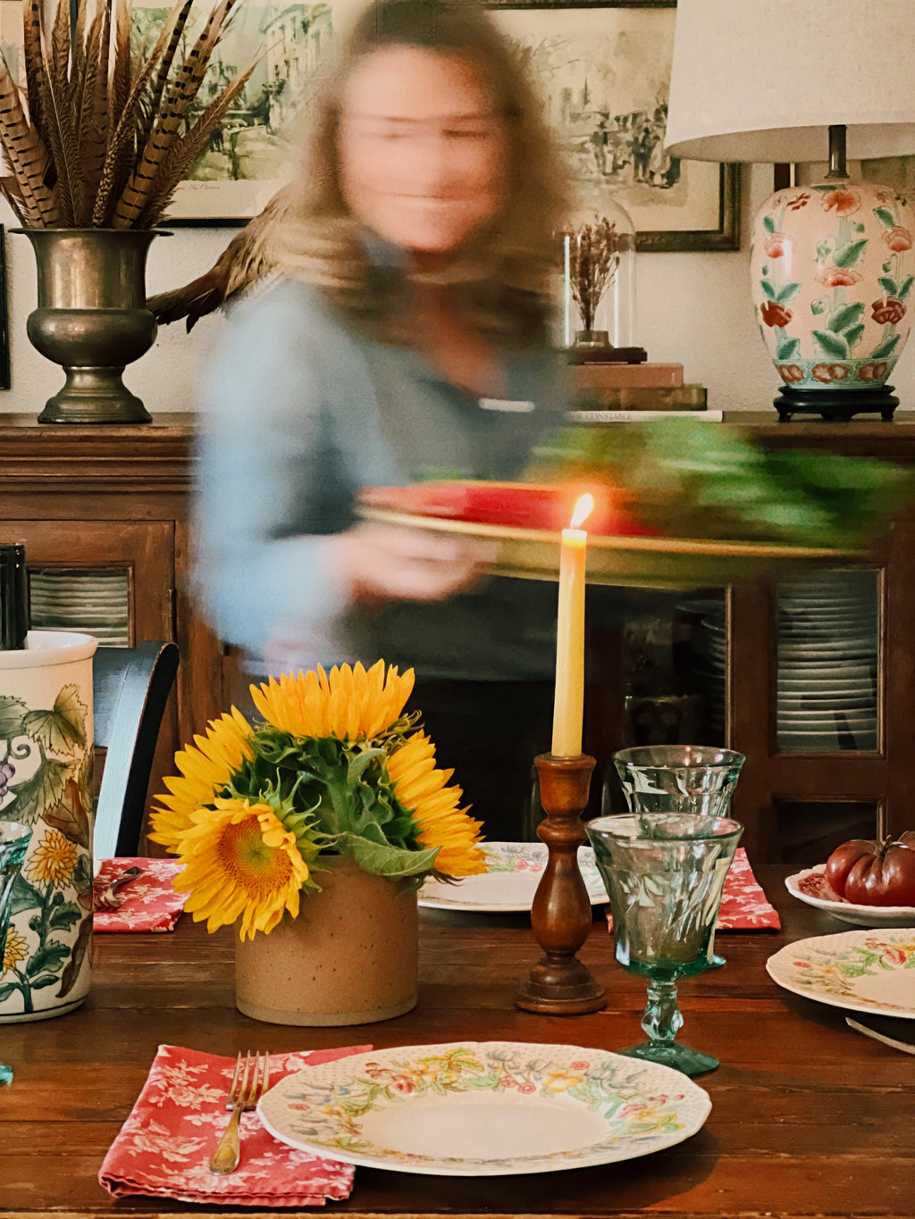 Person holding a tray with a candle and sunflowers on a table in a decorated room.