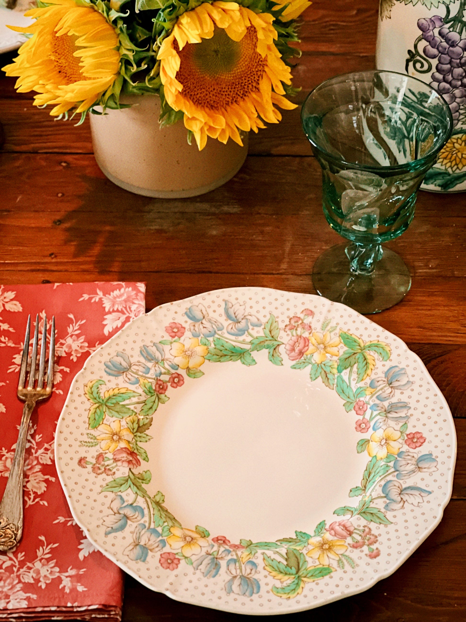Overhead view of a vintage plate with floral design on a wooden table with sunflowers and a glass.