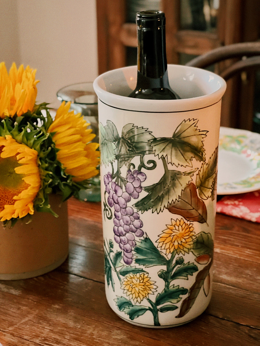 Wine bottle in a decorative ceramic holder with floral patterns on a wooden table.