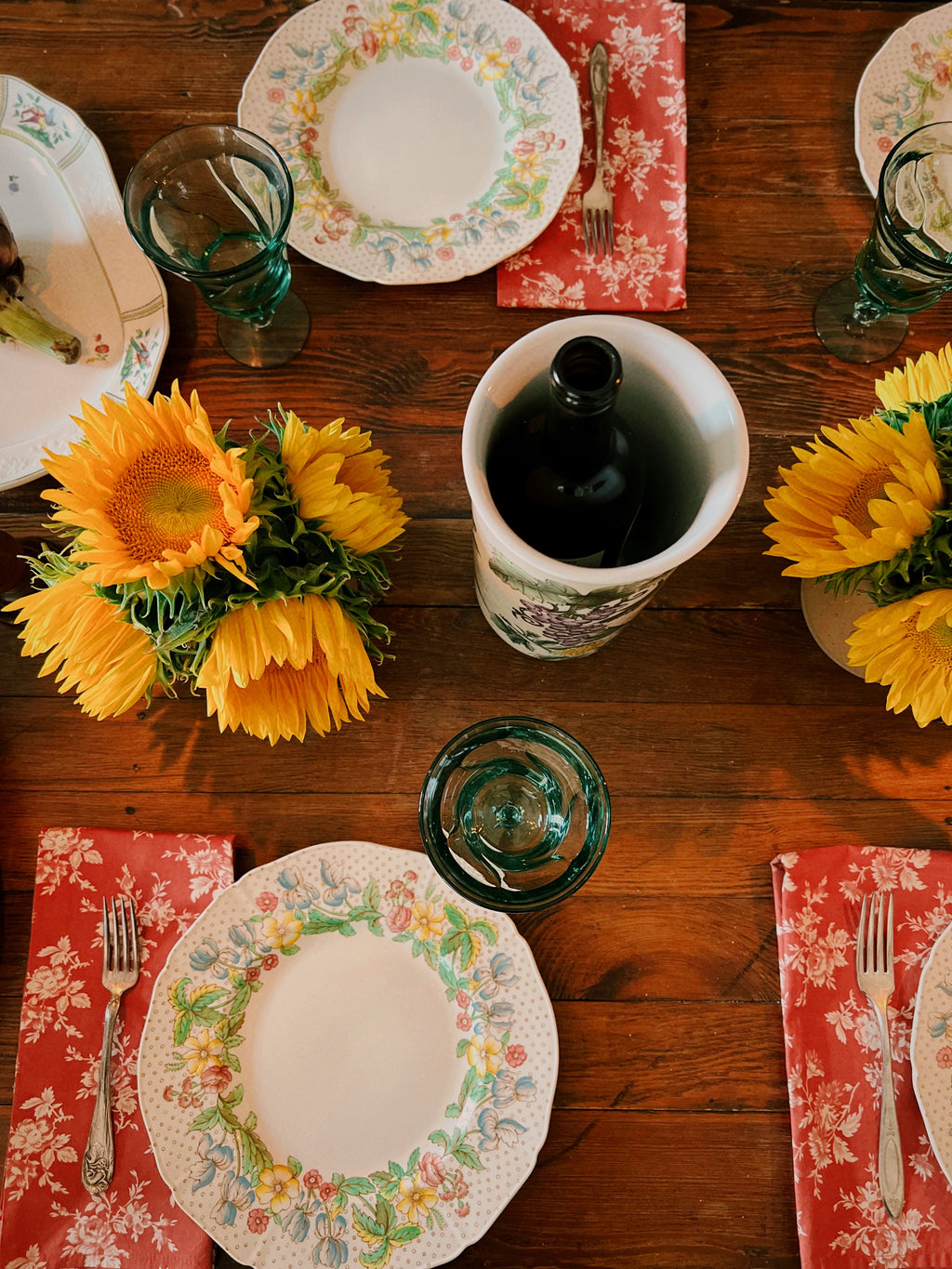 Set table with floral plates, sunflowers, and red Williams Sonoma chintz napkins on a wooden surface.