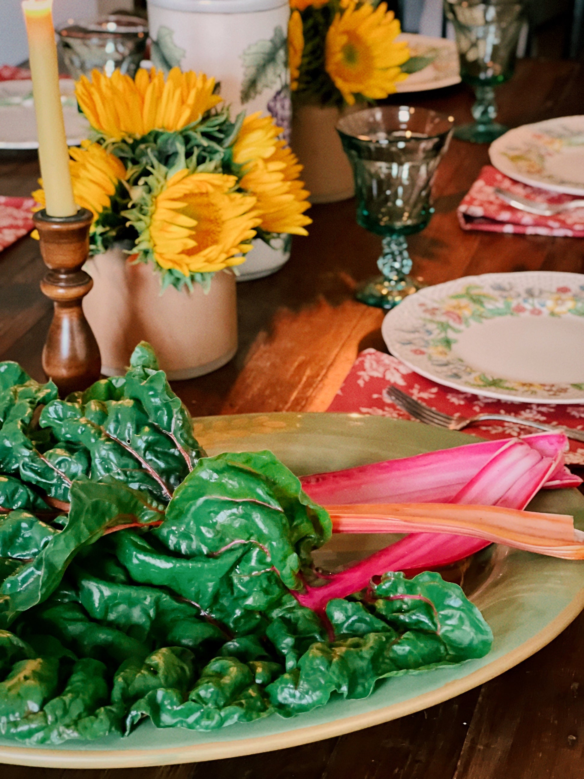 Dinner table setting with green leafy vegetables, yellow flowers, and colorful plates.