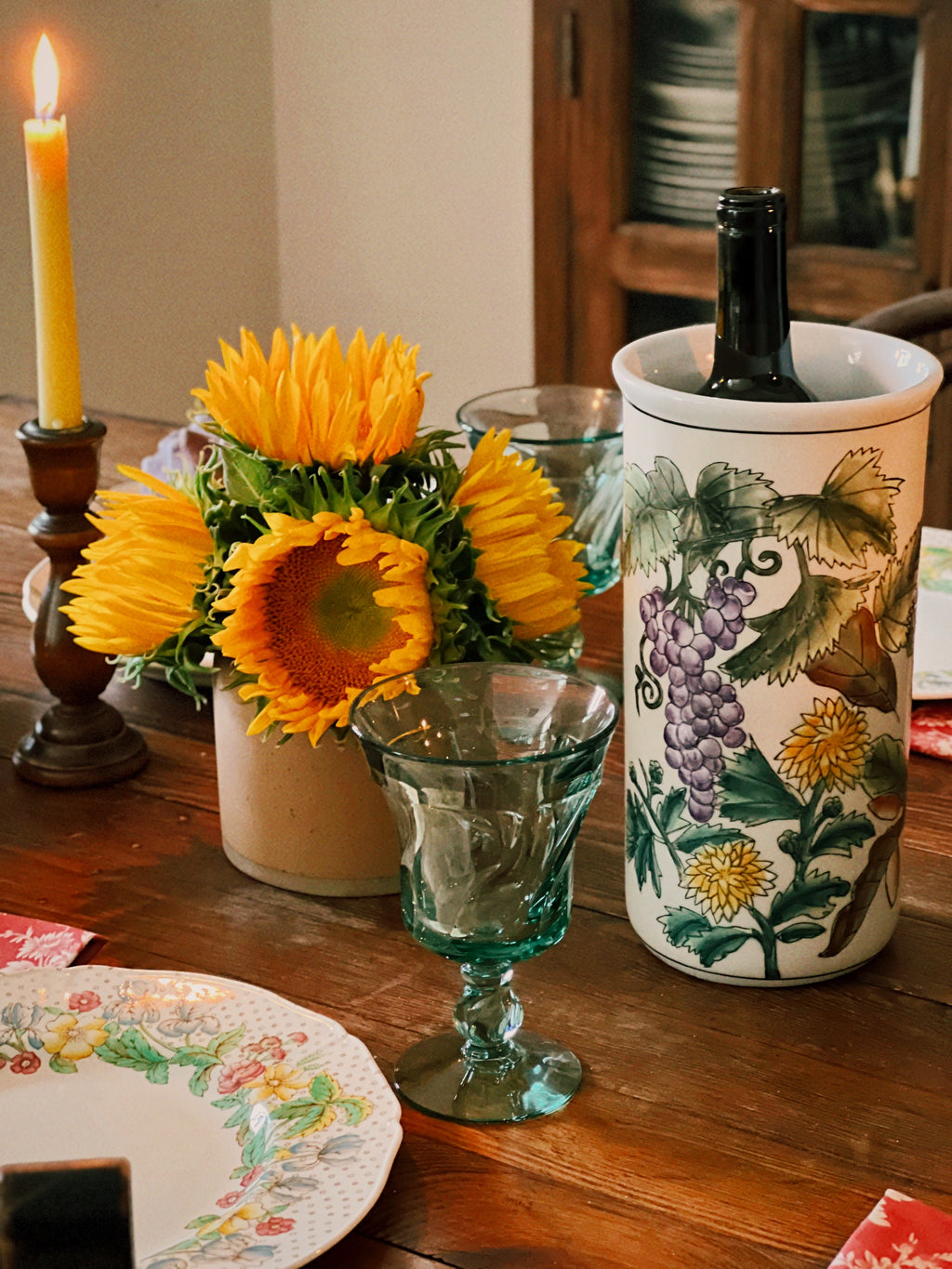 Decorative table setting with sunflowers, a wine bottle in a decorative holder, and a candle.
