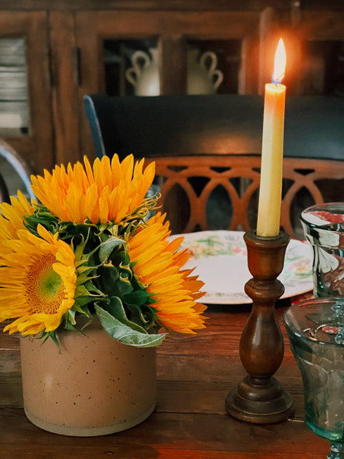 Sunflowers in a vase with a lit candle on a wooden table.