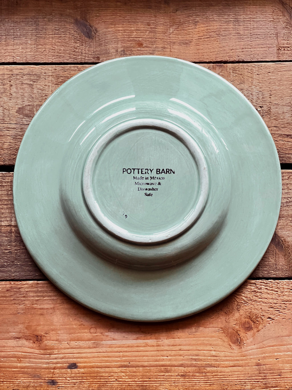 Underside of a Sausalito Sage Green plate with 'Pottery Barn' branding on a wooden surface