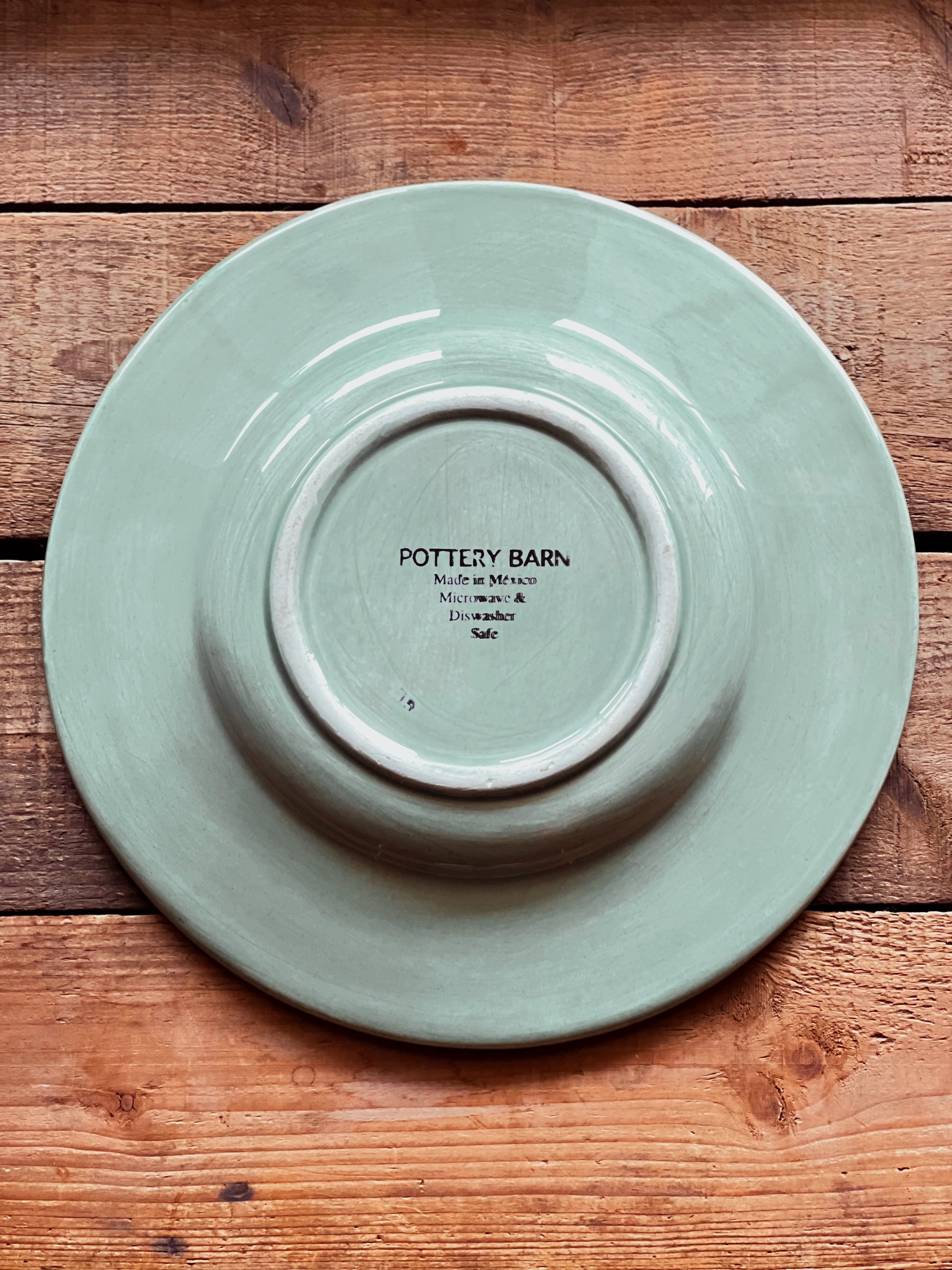 Underside of a Sausalito Sage Green plate with 'Pottery Barn' branding on a wooden surface