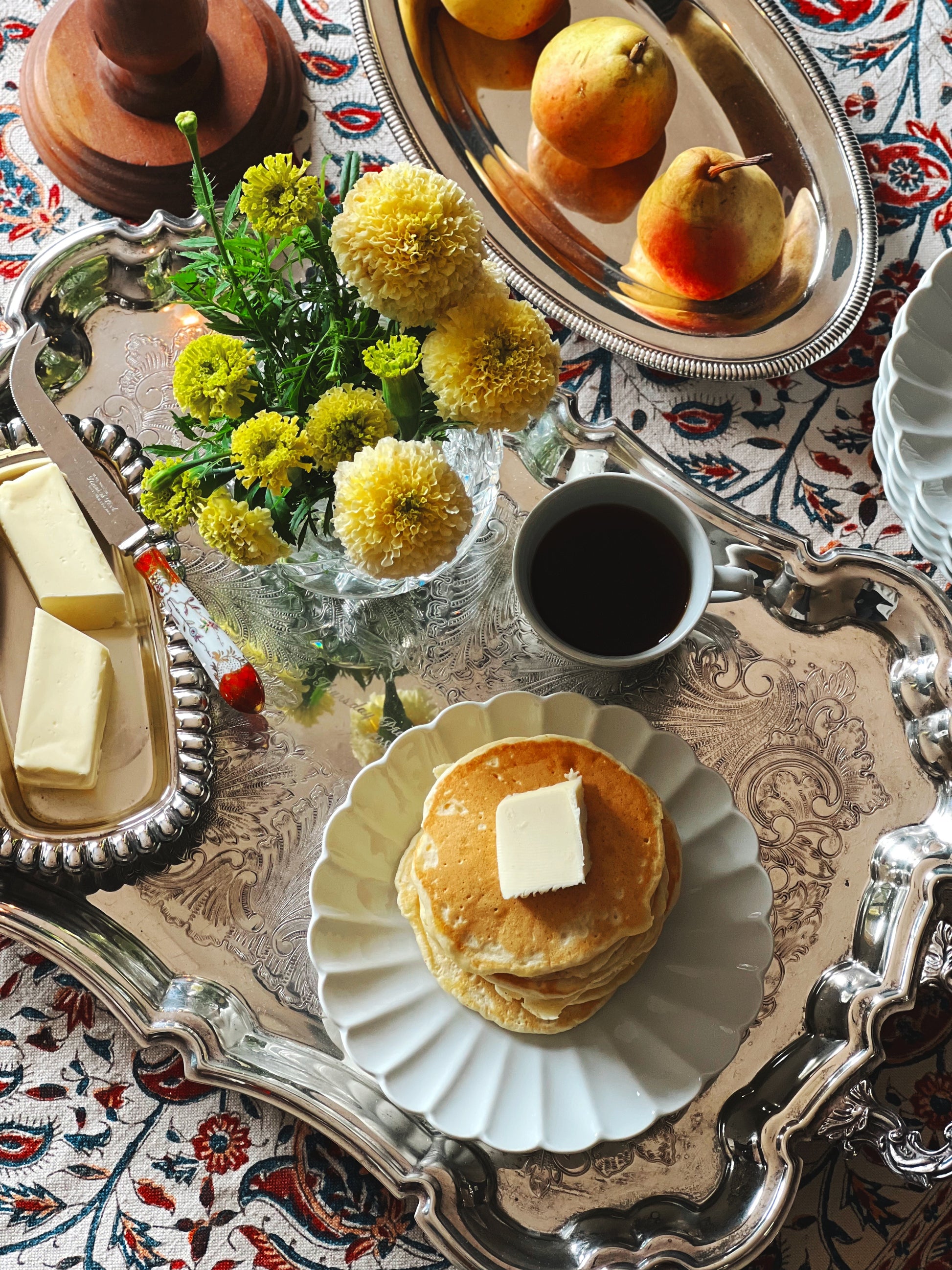 Stack of pancakes with butter on a decorative tray with flowers and coffee.