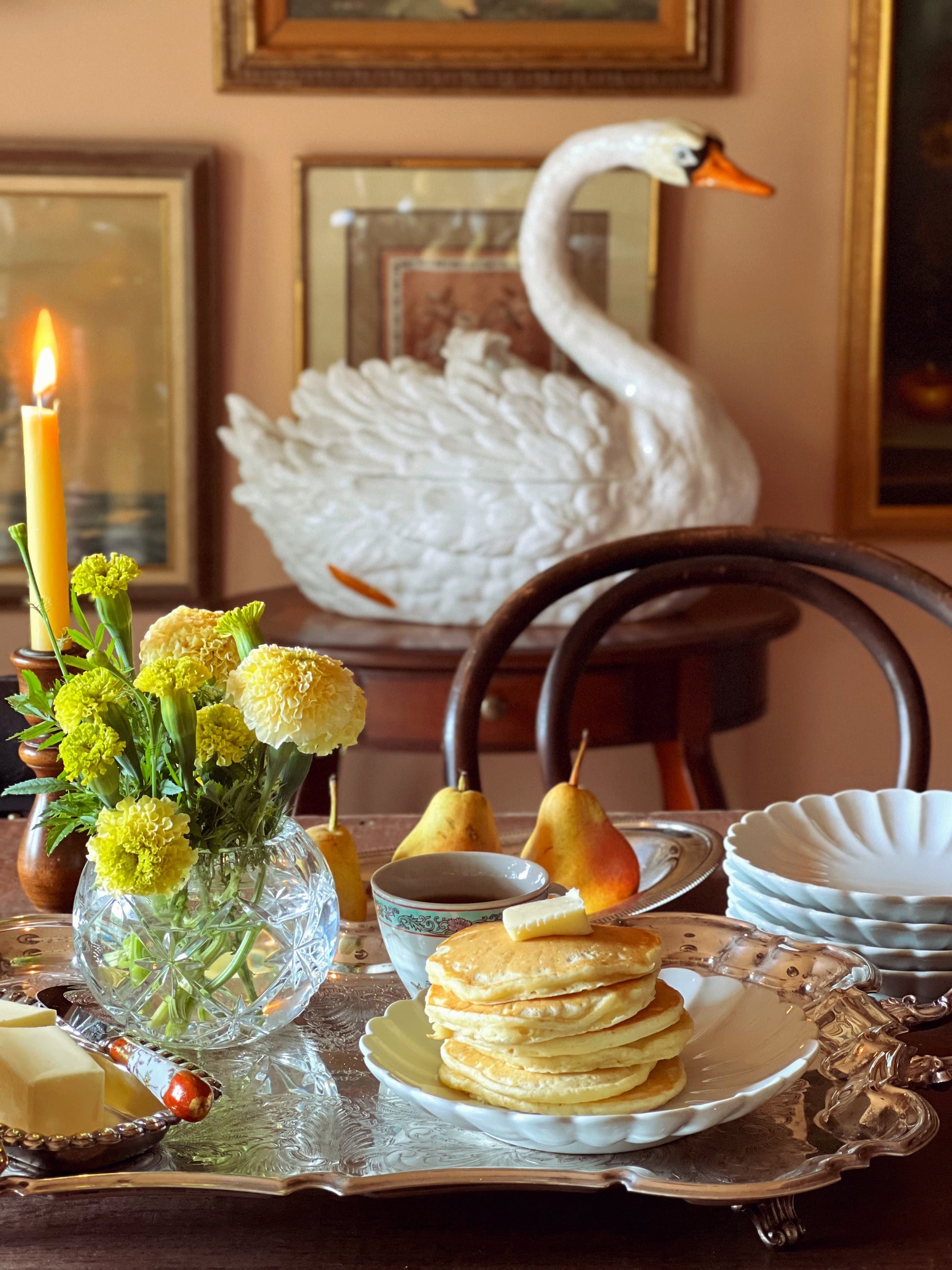 Dining table with pancakes, flowers, and a swan decoration in a home setting.