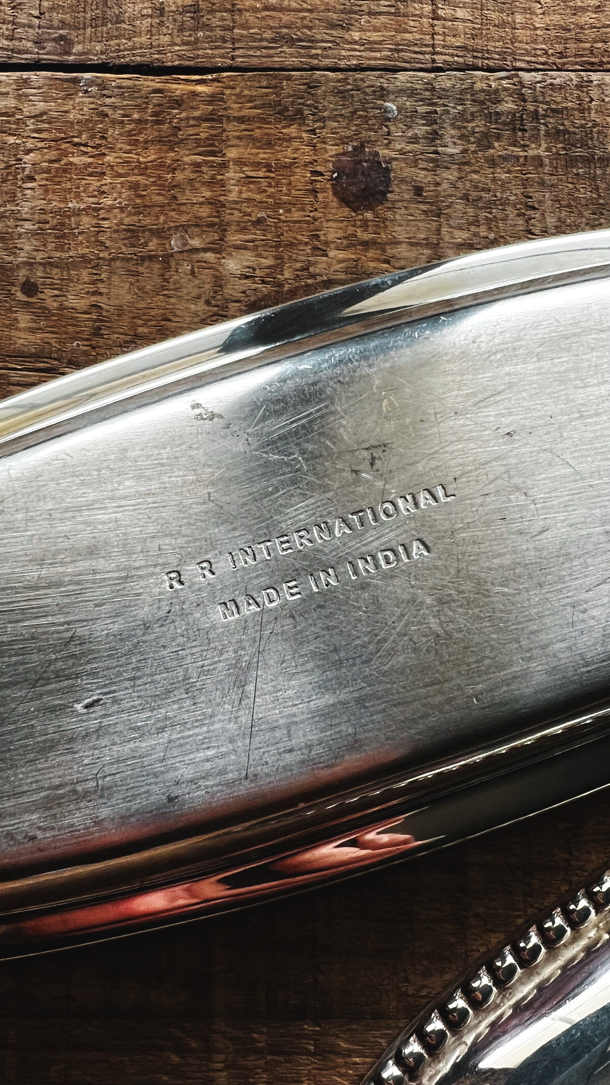 Metal object with 'R & R International Made in India' engraving on a wooden surface