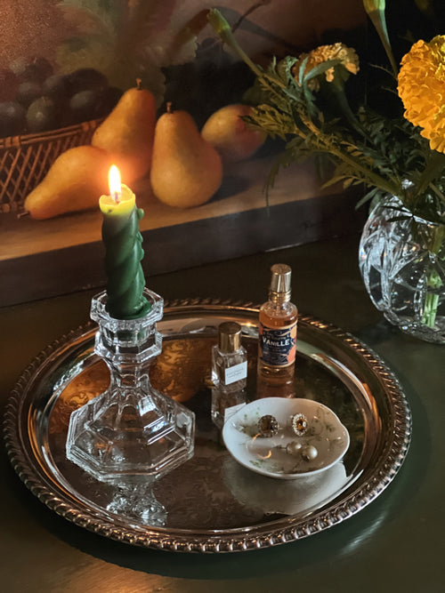 Candlelit scene with a glass candlestick, bottle, and small bowl on a silver tray.