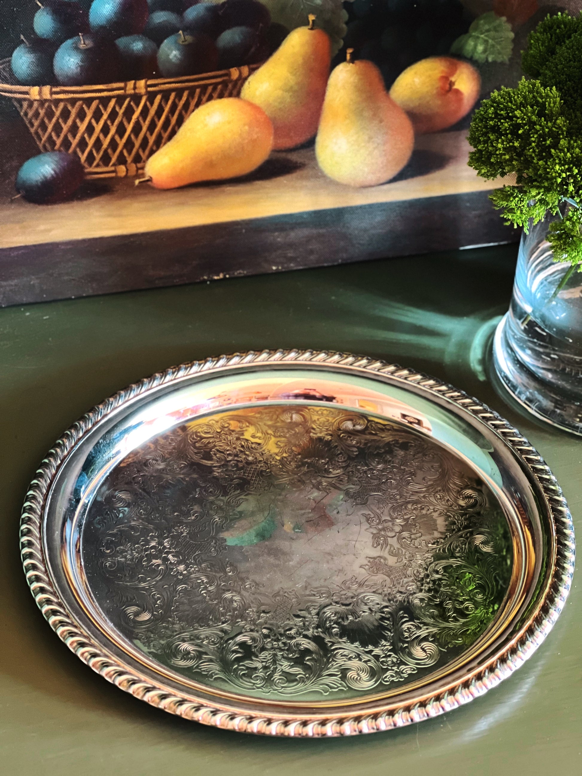 Silver tray on a green surface with fruit in the background