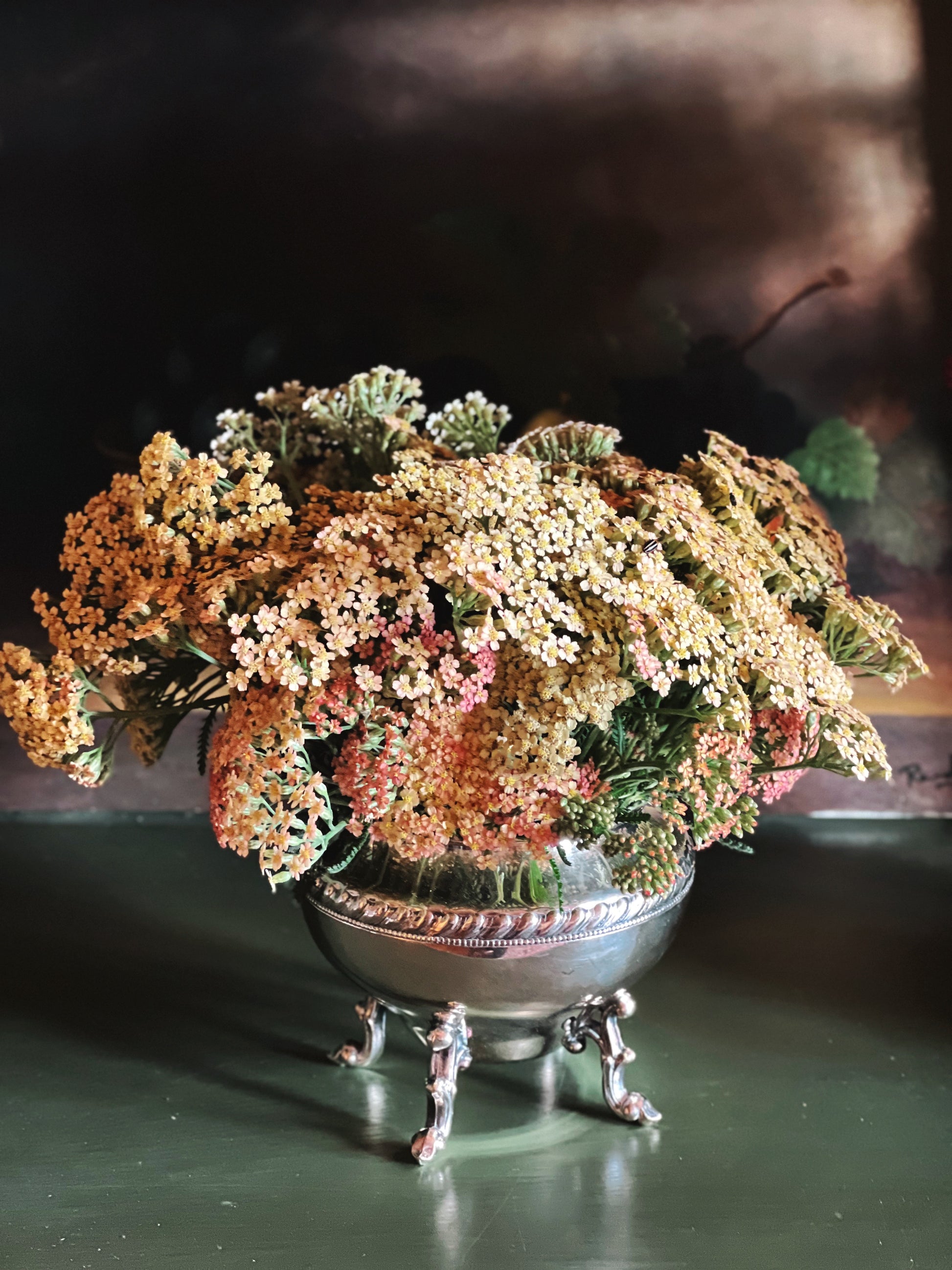 Decorative floral arrangement in a silver bowl on a dark surface
