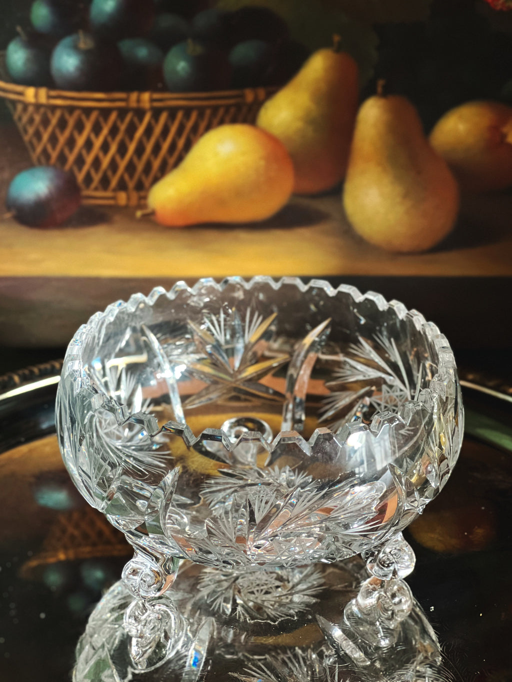 Crystal bowl with intricate designs on a wooden surface with pears and plums in the background.