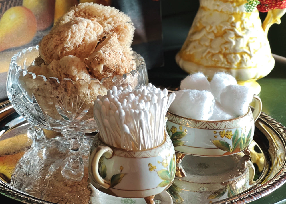 Decorative setting with a glass bowl of seas sponges, a vase of flowers, and ceramic items on a tray.