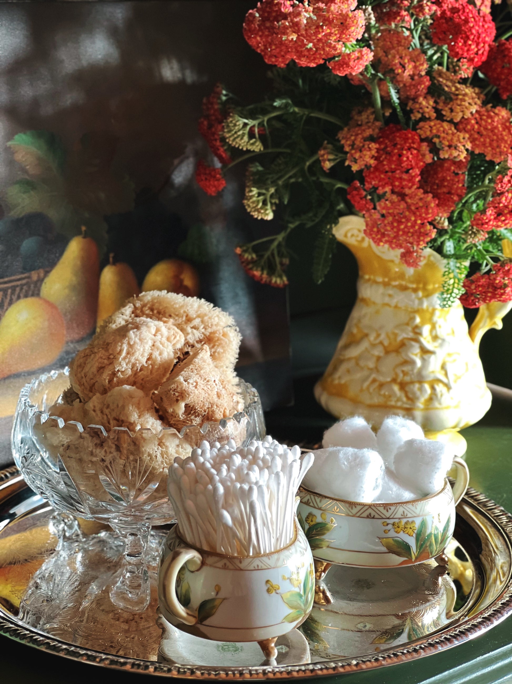 Decorative setting with a glass bowl of sea sponges, a vase of flowers, and ceramic items on a tray.